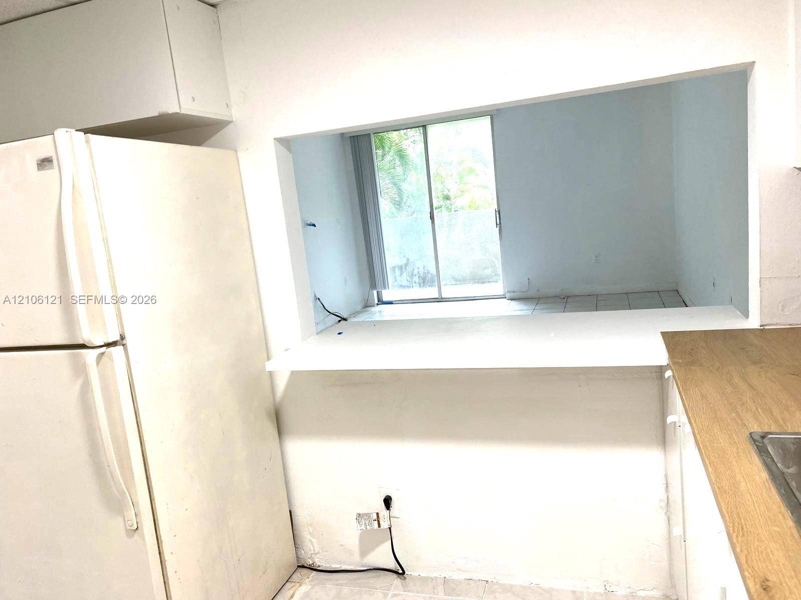 Kitchen featuring a pass-through counter, white cabinetry, wood-finish countertop, and white refrigerator