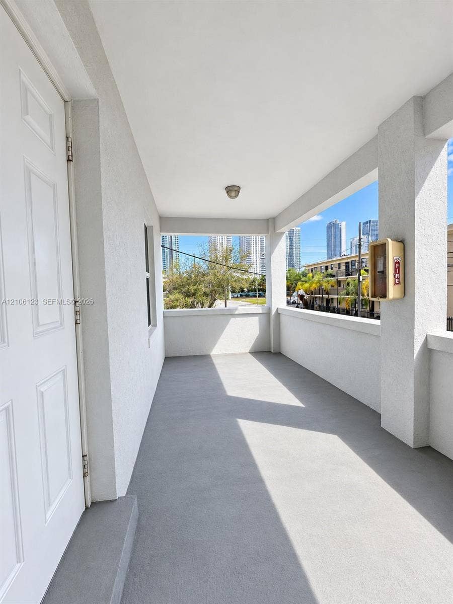 123 NW 15th Street, #U, Miami, Miami, FL 33136 Covered balcony featuring a neutral-toned concrete floor, textured wall finishes, and a high ceiling with a flush-mount light fixture