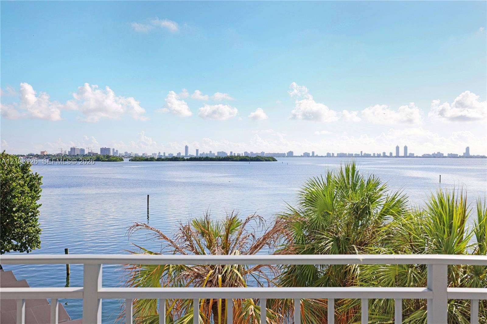 Elevated balcony featuring a white railing, overlooking open water and a distant cityscape skyline