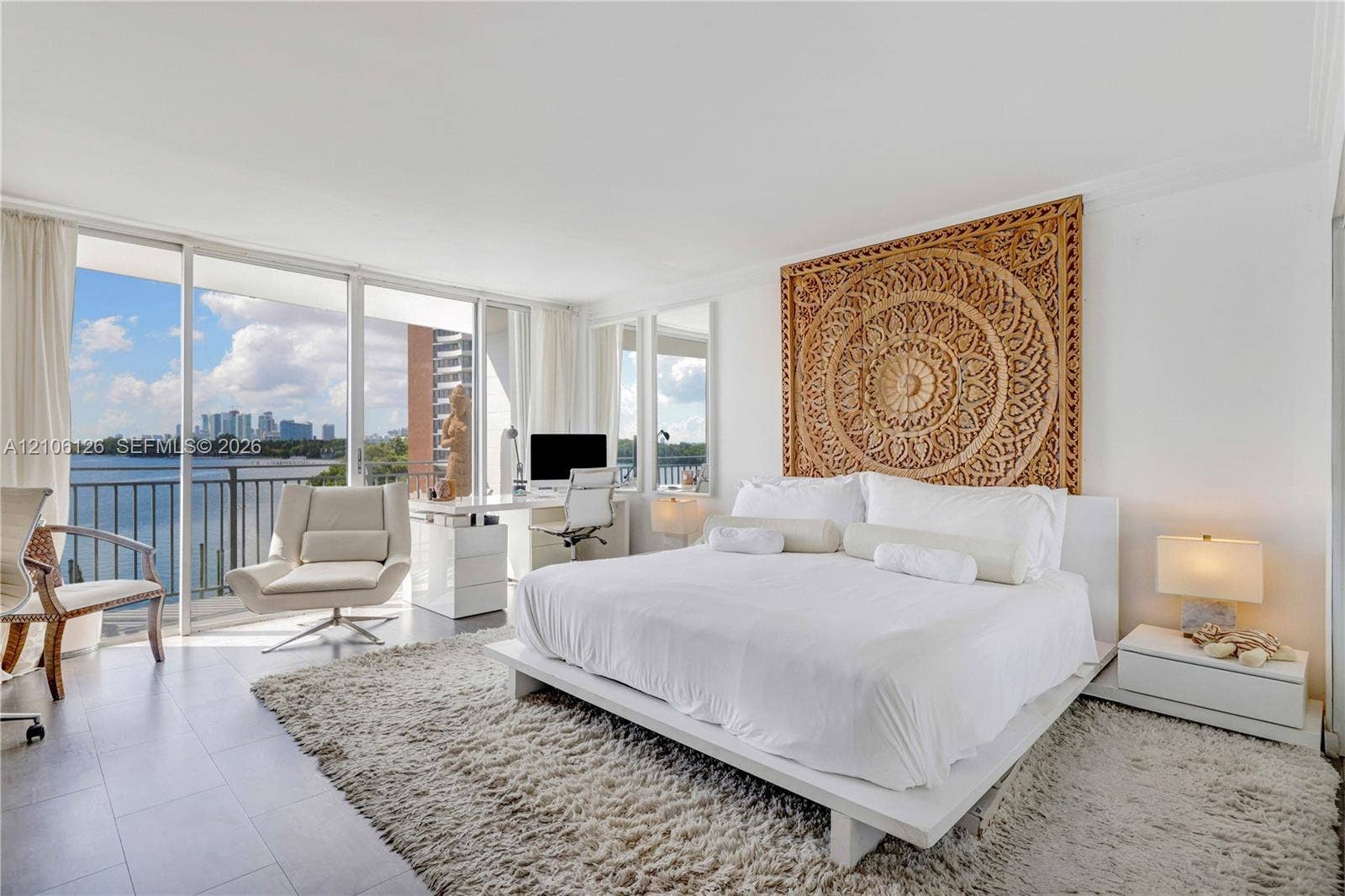 Floor-to-ceiling sliding glass doors, white tile flooring, and a private balcony featuring a water-front backdrop