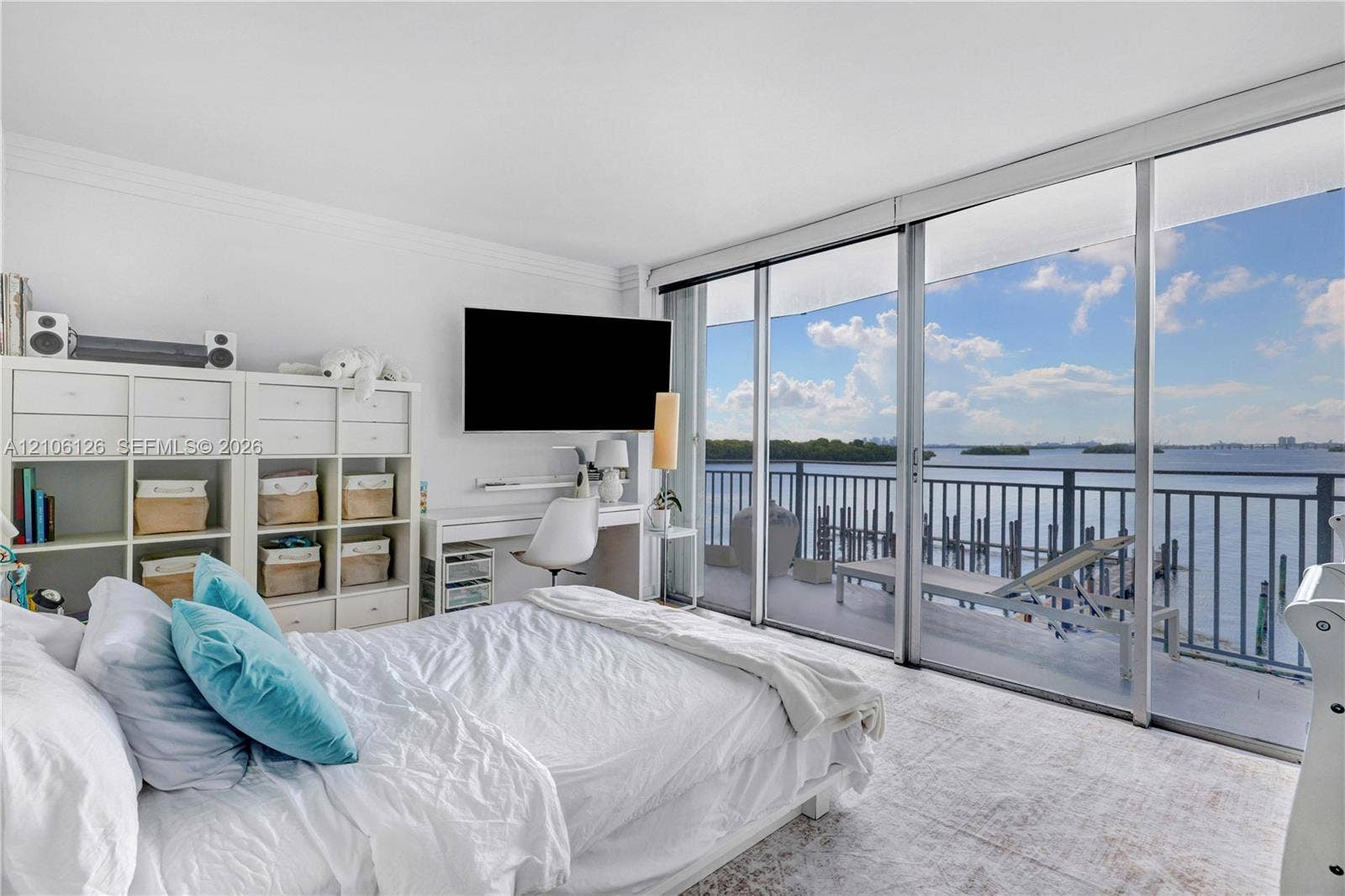 Floor-to-ceiling glass sliding doors opening to an expansive balcony with metal railing, carpeting, and water scenery