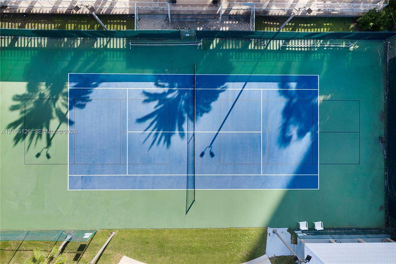 Tennis court featuring a hard surface with green and blue court markings, perimeter fencing, and integrated lighting fixtures