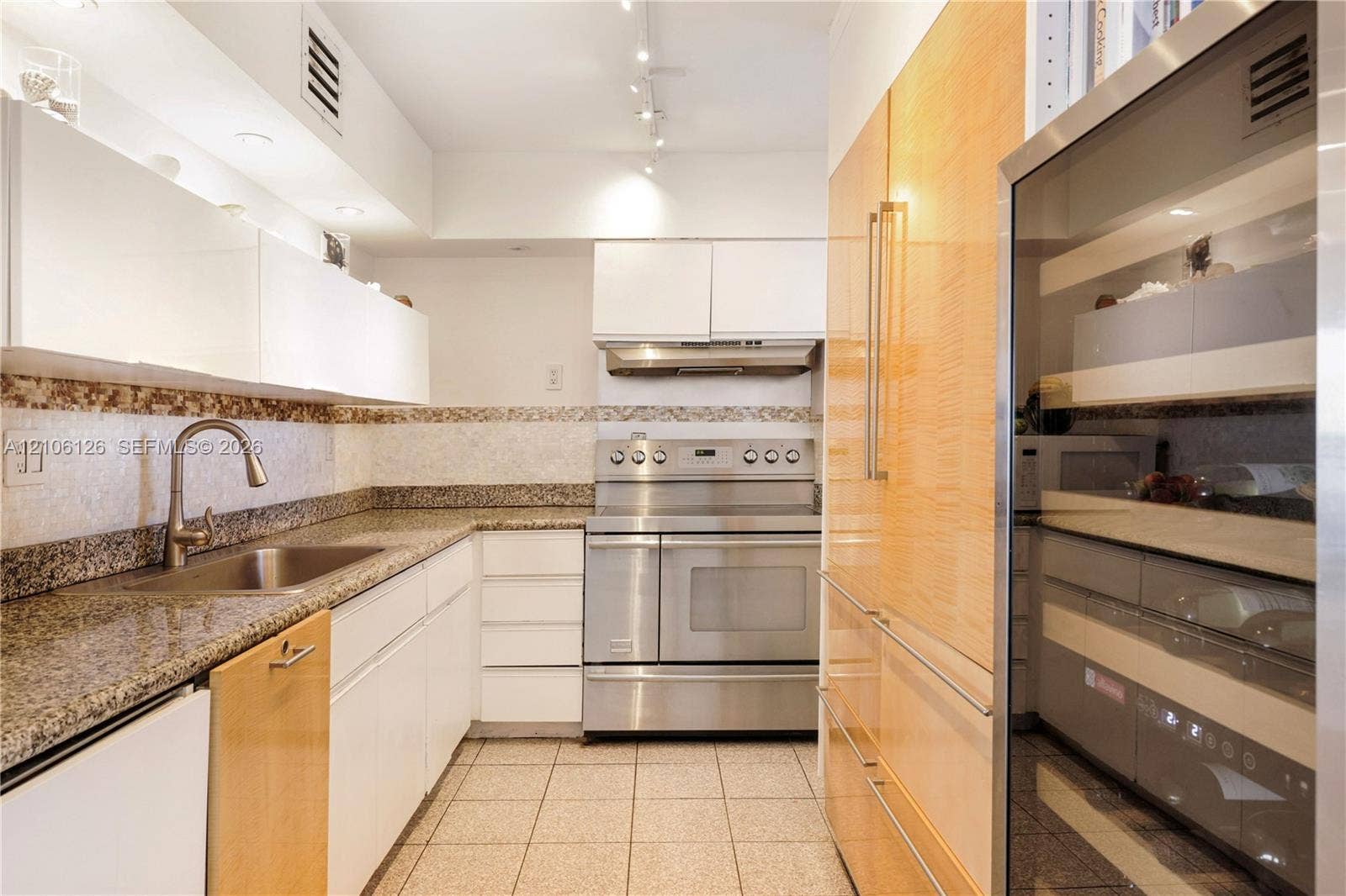 Kitchen featuring stainless steel appliances, stone countertops, custom cabinetry with wood and white finishes, tile flooring, and a stainless steel undermount sink