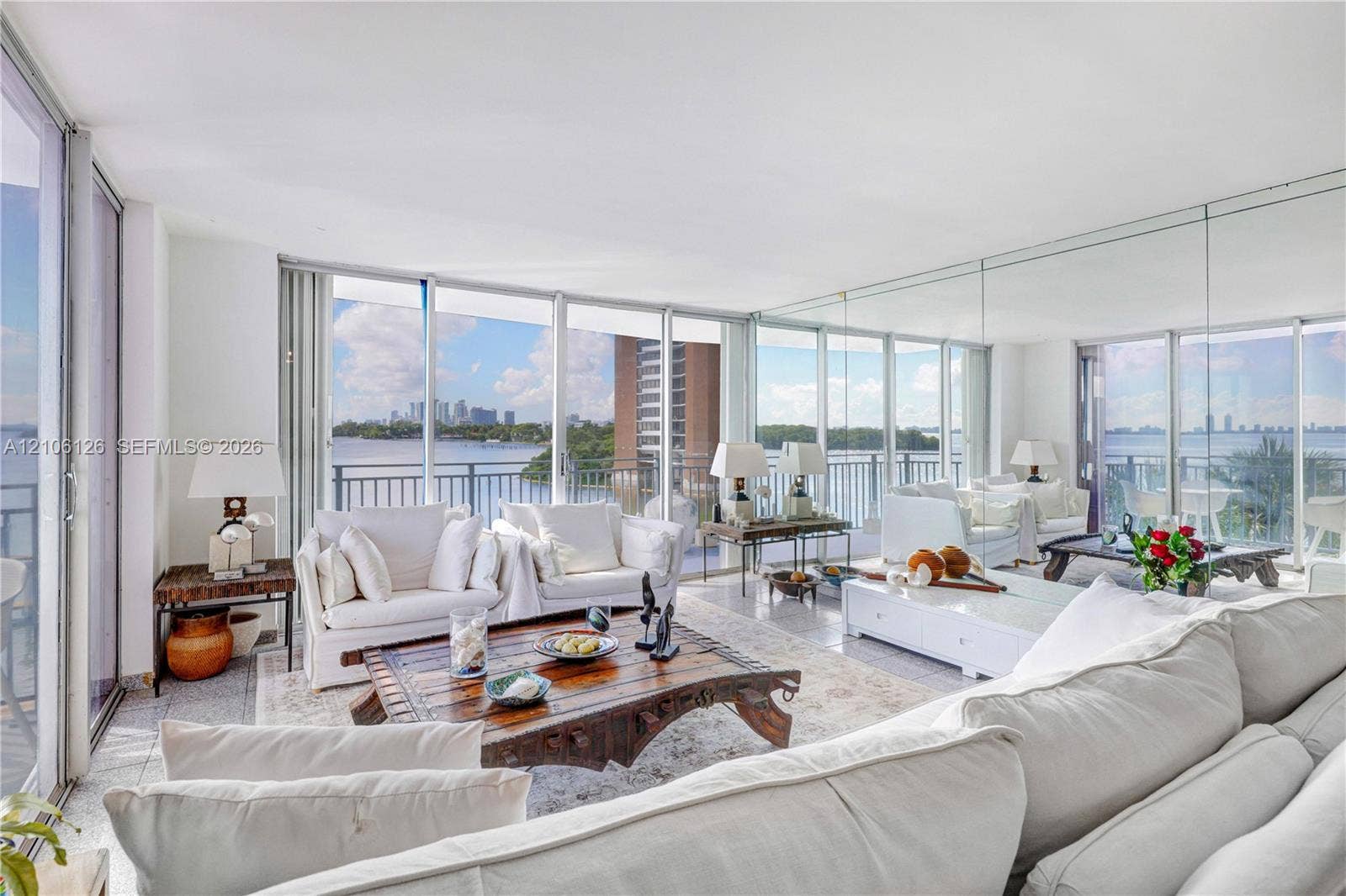 Floor-to-ceiling glass walls, integrated mirrored wall panels, stone-finish flooring, and private balcony access with water backdrop