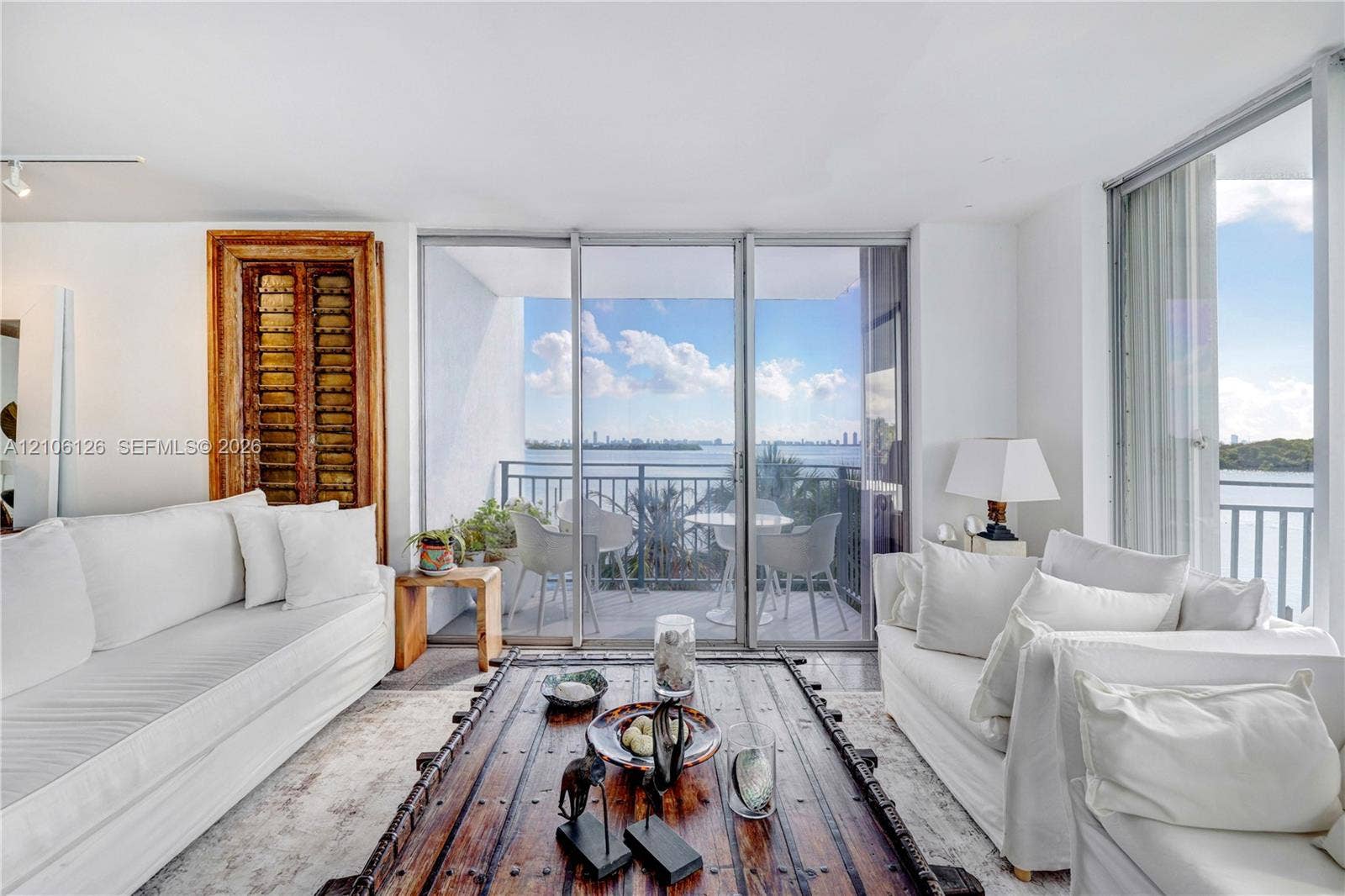 Floor-to-ceiling glass sliding doors, private balcony, water backdrop, and white walls