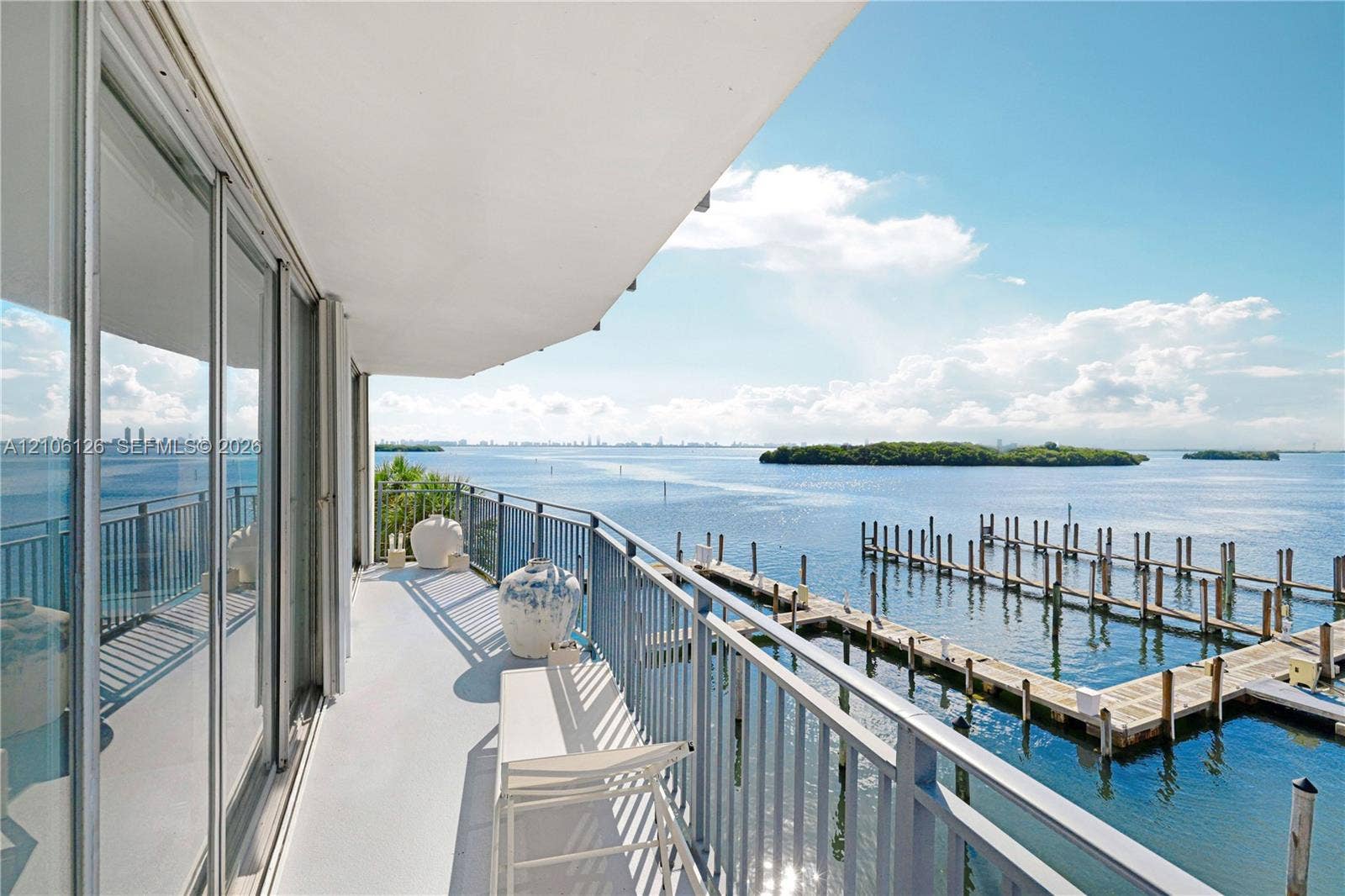 Covered balcony with a protective metal railing, floor-to-ceiling glass sliding doors, and water frontage featuring a private dock system