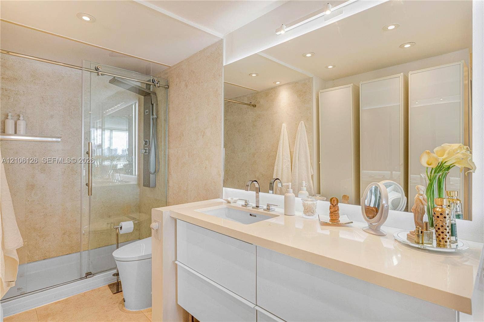 Modern bathroom featuring a wall-mounted floating vanity with a stone countertop, dual chrome faucets, a glass-enclosed walk-in shower with stone tile wall surfacing, and floor-to-ceiling built-in cabinetry