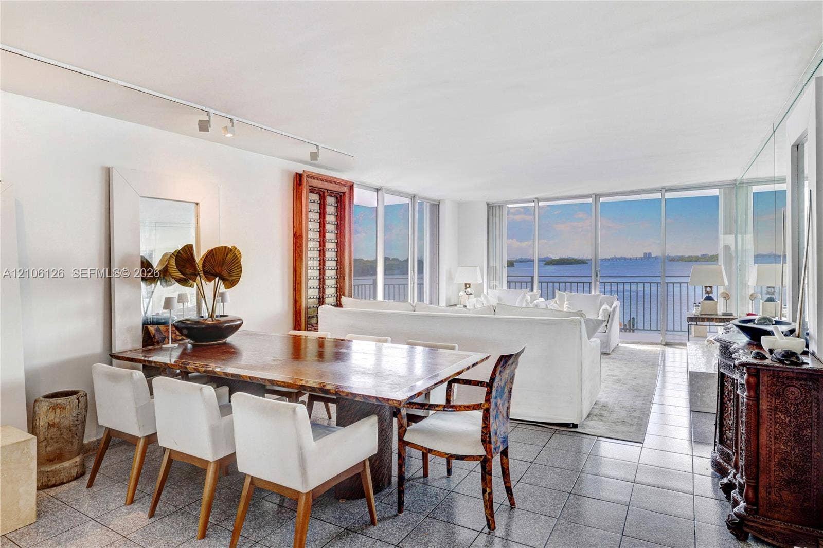 Open-concept living space featuring floor-to-ceiling windows, panoramic water scenery, polished stone-tile flooring, and adjustable ceiling-mounted track lighting