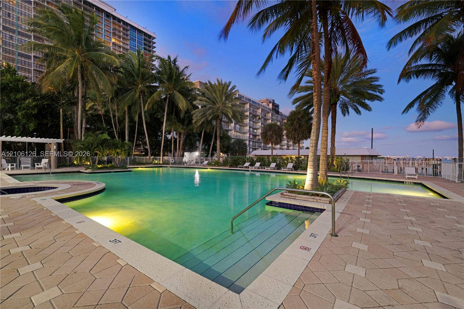In-ground swimming pool featuring a built-in spa, paved stone decking, metallic handrails, and tropical landscaping