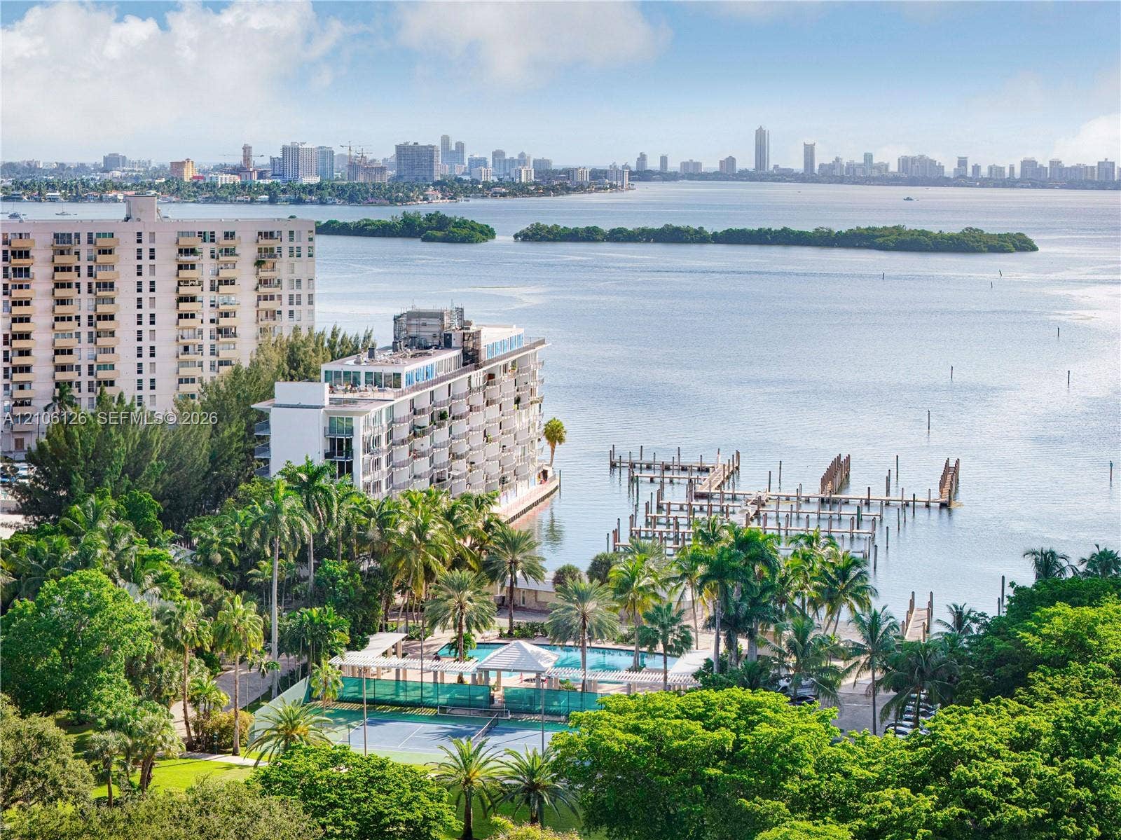 Waterfront complex featuring a private boat dock, outdoor swimming pool, tennis court, and mature tropical landscaping