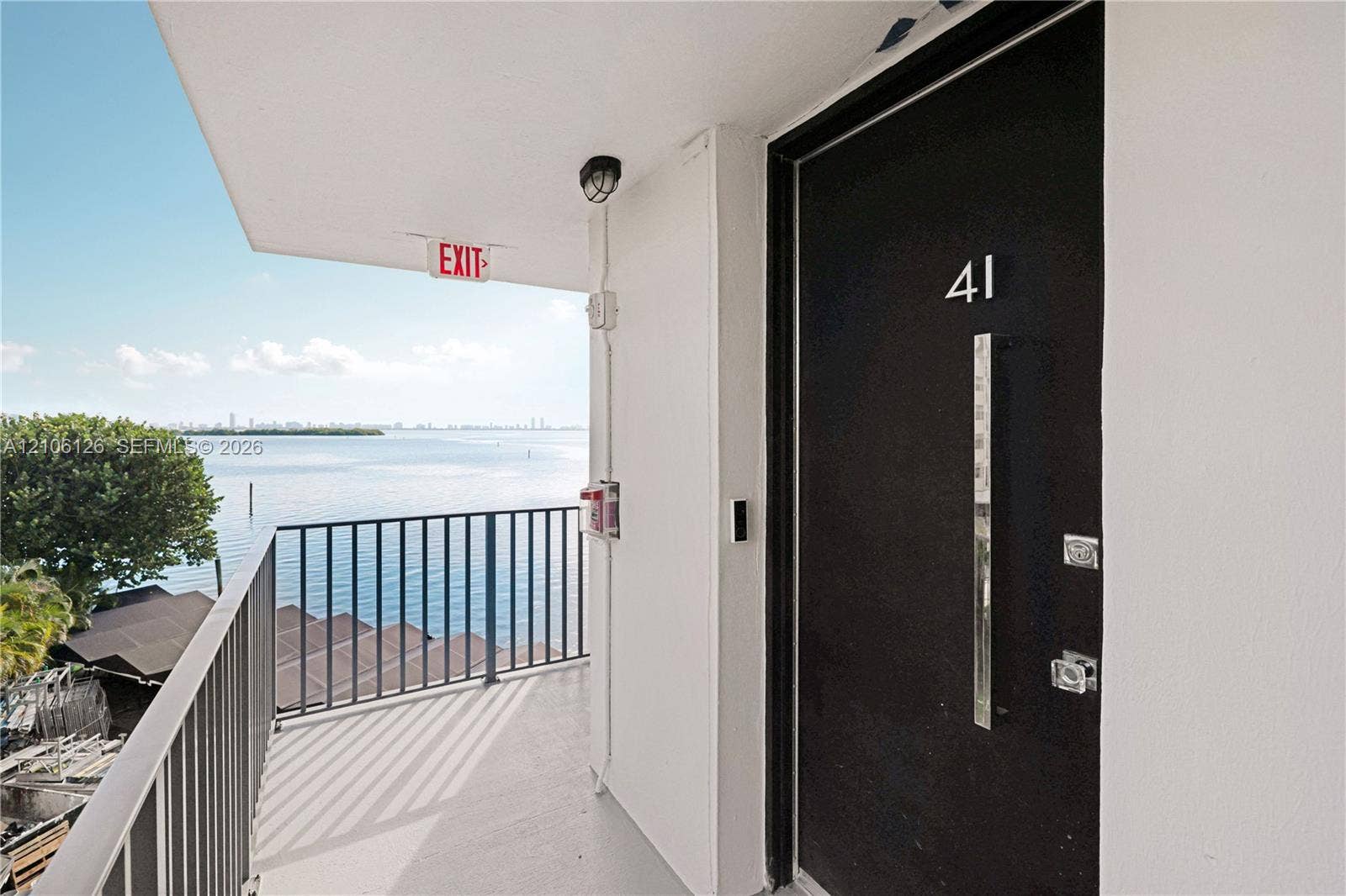 Exterior entryway featuring a dark-toned door with a modern vertical pull handle, recessed ceiling lighting, and a metal balcony railing overlooking the water