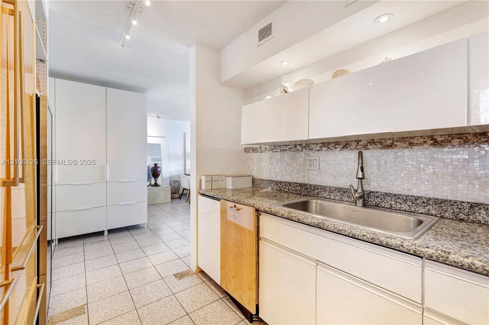 Kitchen featuring white flat-panel cabinetry, stone countertops, stainless steel undermount sink with a gooseneck faucet, mosaic tile backsplash, and light-toned ceramic tile flooring