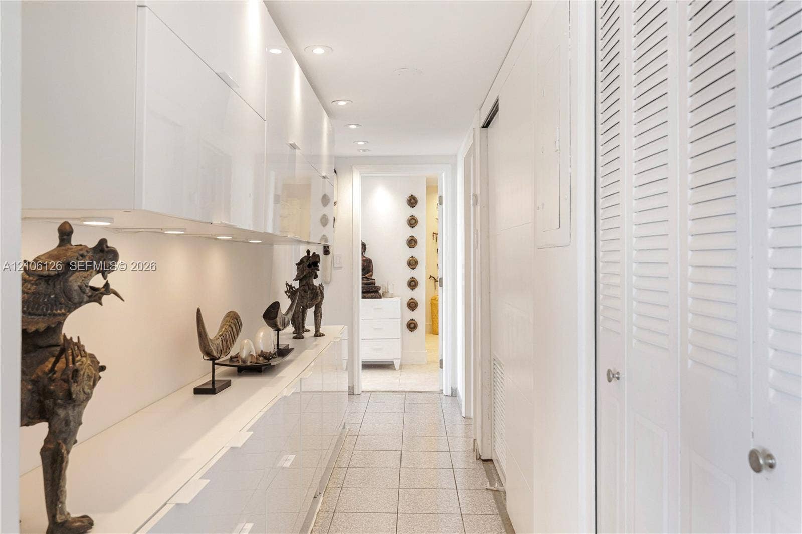 Hallway featuring high-gloss white built-in cabinetry, recessed ceiling lighting, tile flooring, and louvered double-door closet