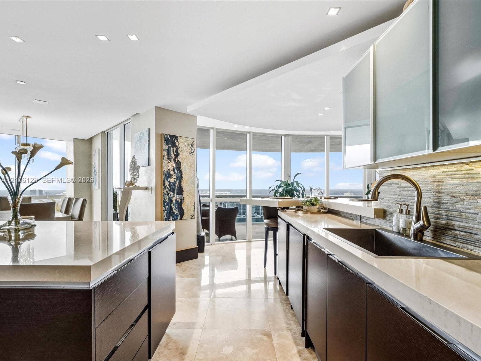 Modern kitchen featuring quartz countertops, dark wood-finish cabinetry, floor-to-ceiling windows, stacked-stone backsplash, and polished stone flooring