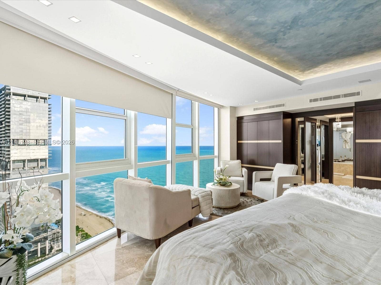 Floor-to-ceiling windows, ocean horizon backdrop, recessed ceiling lighting with painted artistic detail, built-in dark wood cabinetry, and polished stone flooring