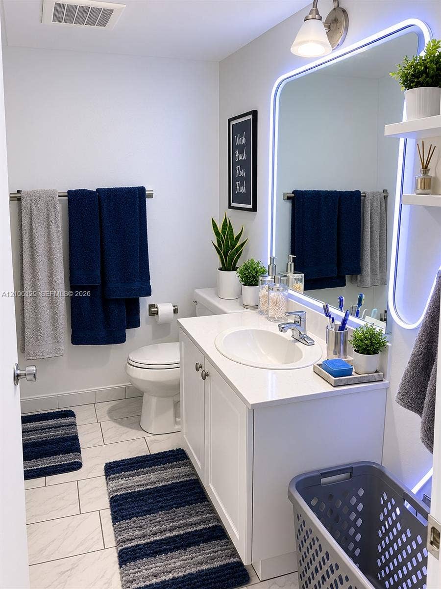 2740 SW 28th Terrace, #307, Miami, FL 33133 White vanity with a rectangular countertop, integrated oval basin, polished chrome faucet, and a large wall-mounted mirror featuring integrated LED perimeter lighting