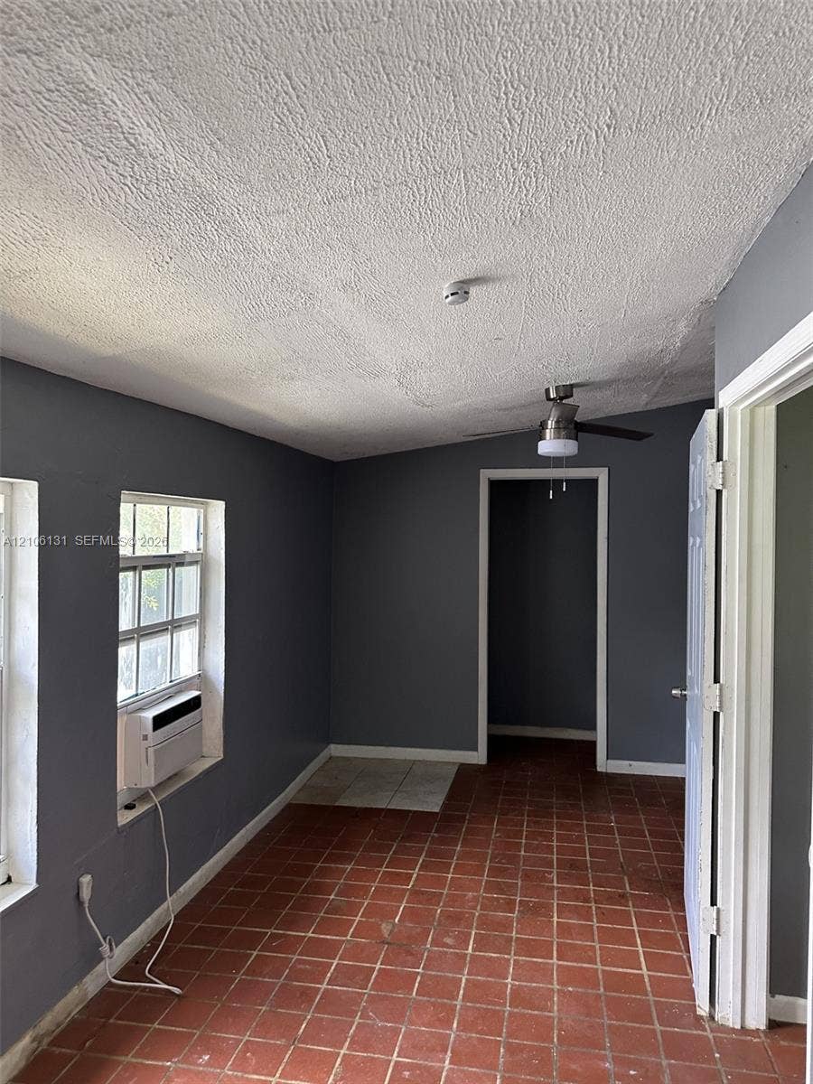 2030 NW 34th Street, Miami, FL 33142 Room featuring red clay tile flooring, gray-toned wall finish, ceiling fan with integrated lighting, and multiple windows