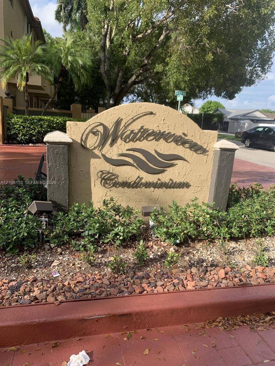Stucco monument signage with dimensional lettering, stone-capped pillars, and decorative landscape beds