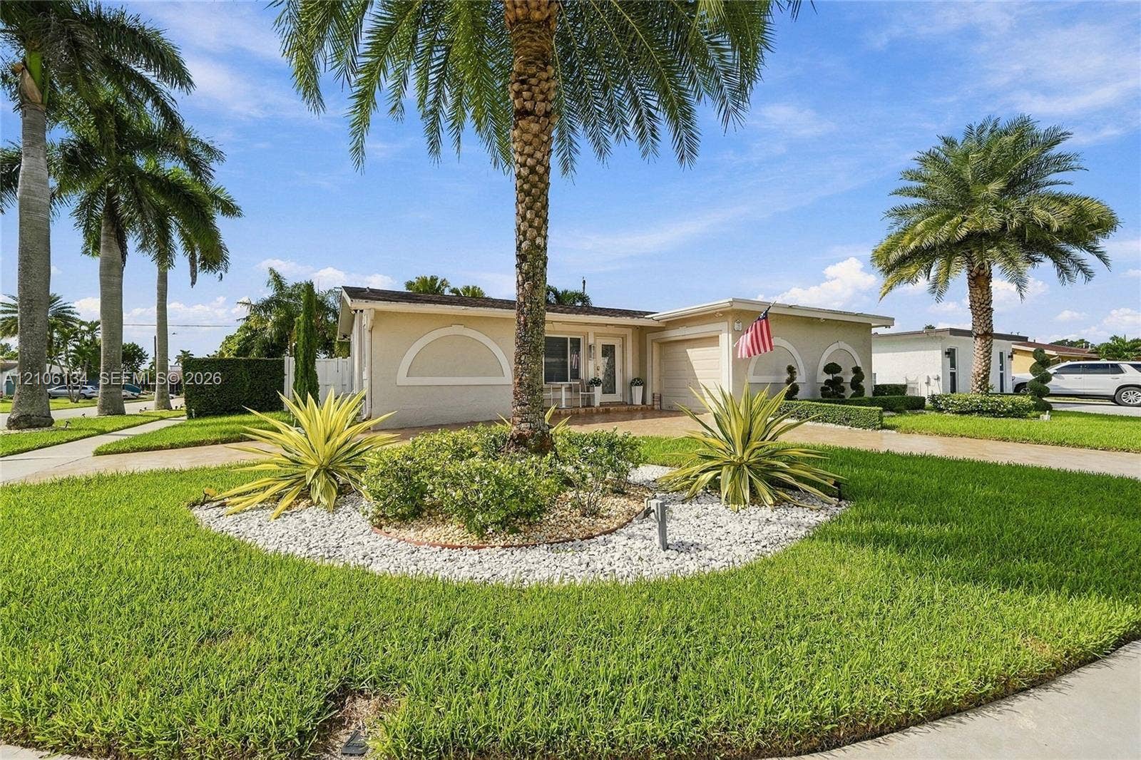 Single-story residence featuring a stucco facade with arched architectural detailing, a paved driveway, and mature palm trees within a landscaped front yard