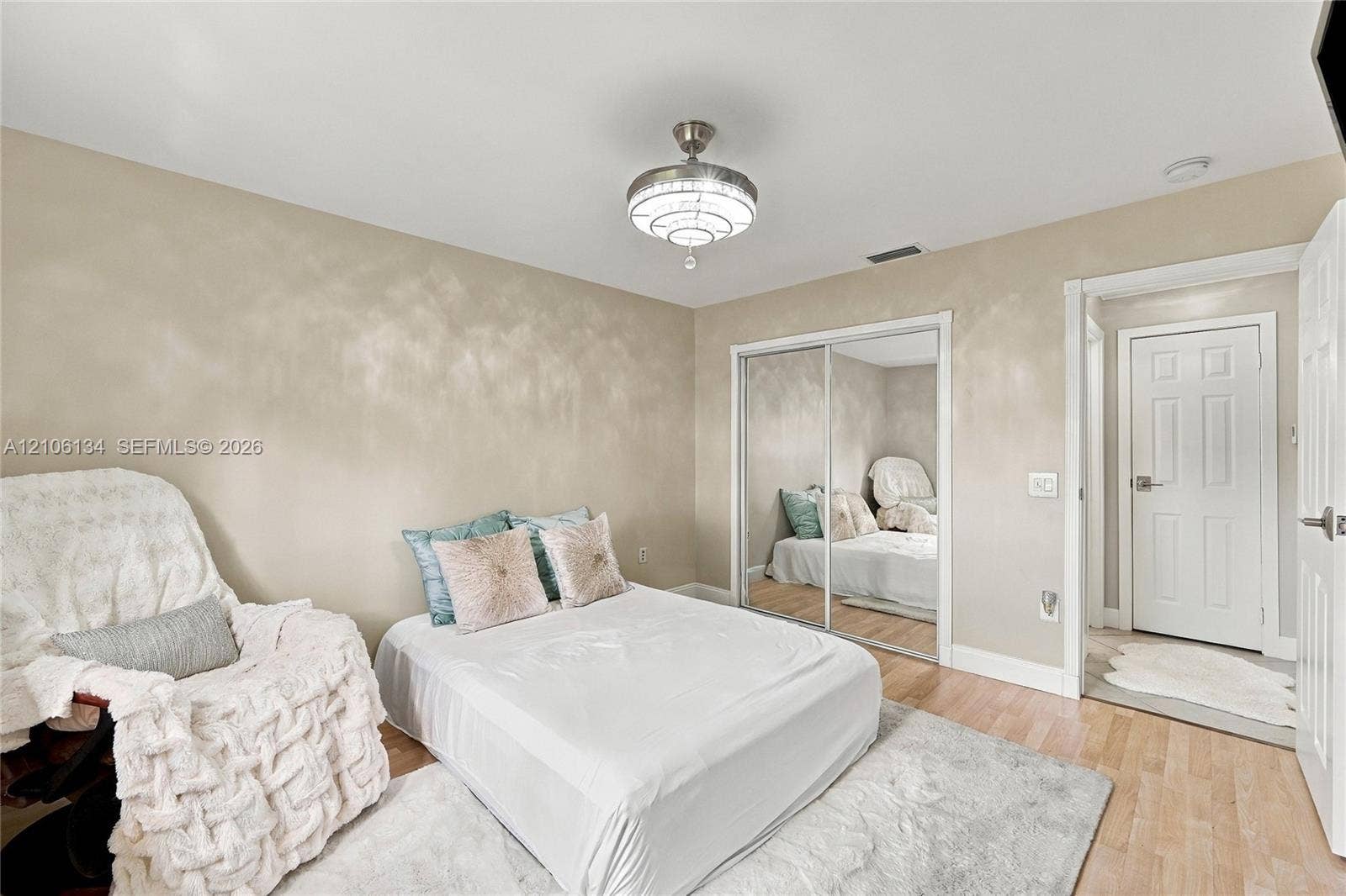 Neutral-toned room featuring wood-finish flooring, a contemporary multi-tiered glass flush-mount light fixture, and floor-to-ceiling mirrored closet doors