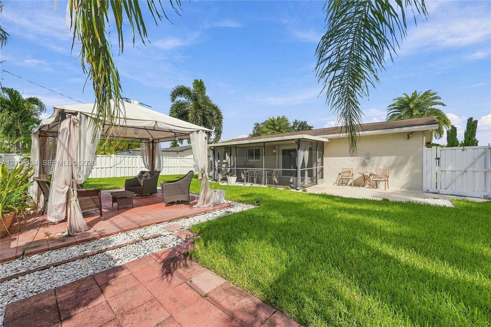 Backyard featuring a paved patio, a metal-framed pergola, a screened-in porch, a white privacy fence, and a manicured lawn