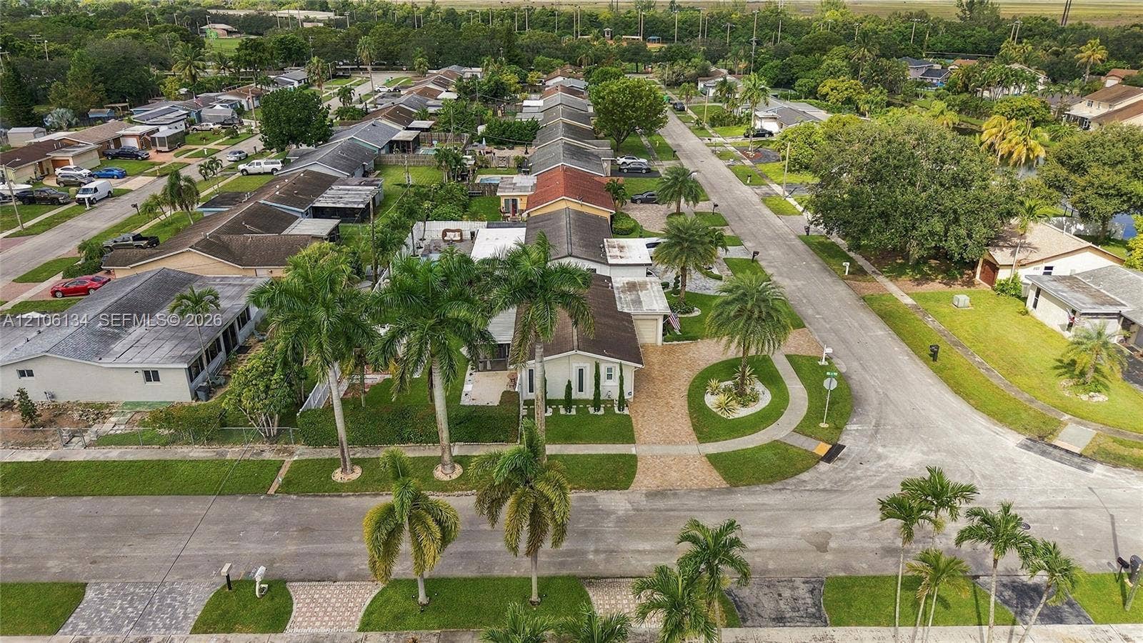 Aerial perspective of the property featuring a paver driveway, mature palm trees, landscaped green space, and residential street access