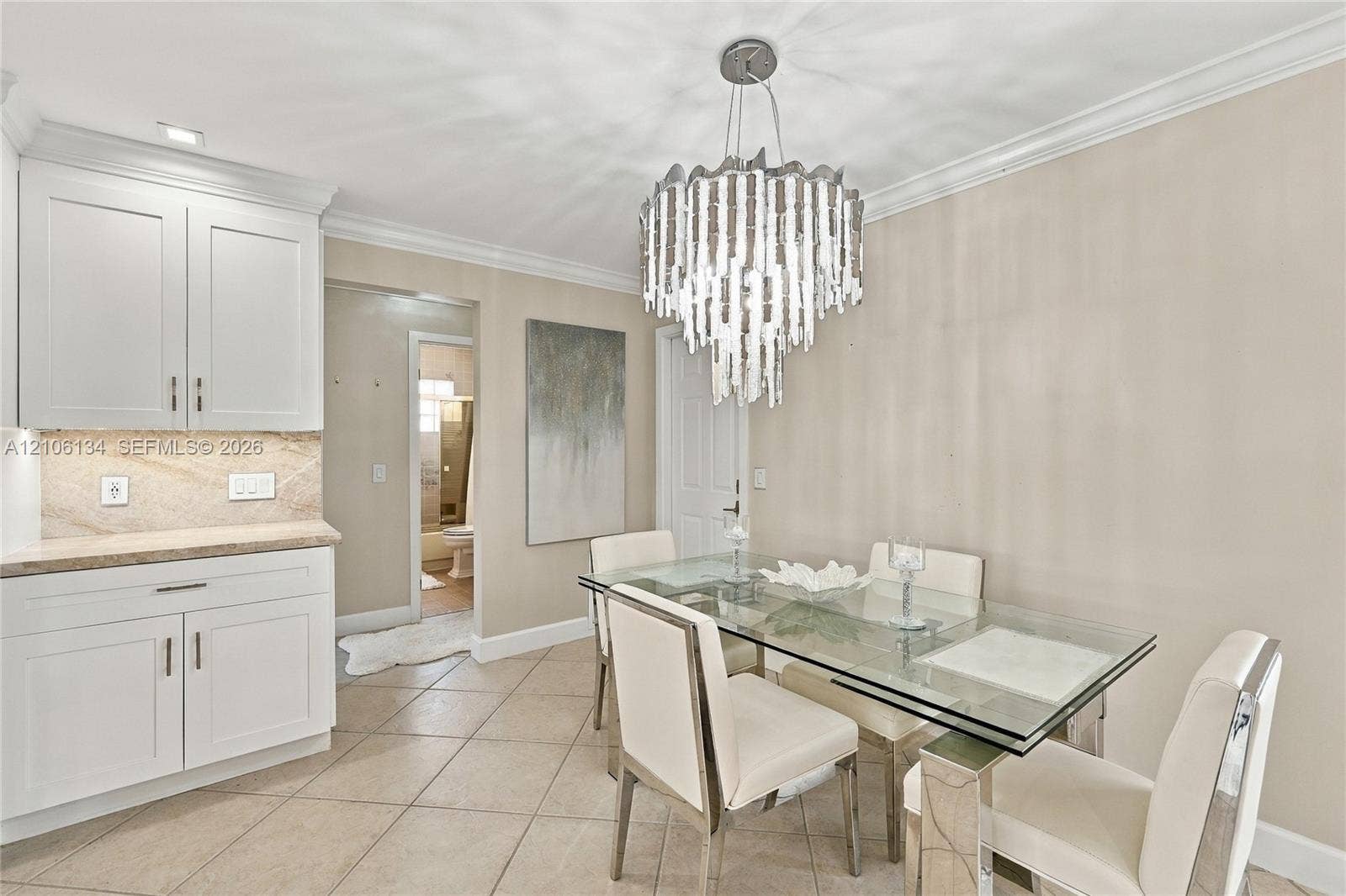 Dining area featuring large-format ceramic tile flooring, custom white cabinetry, stone-surface countertops, and a multi-tiered crystal chandelier