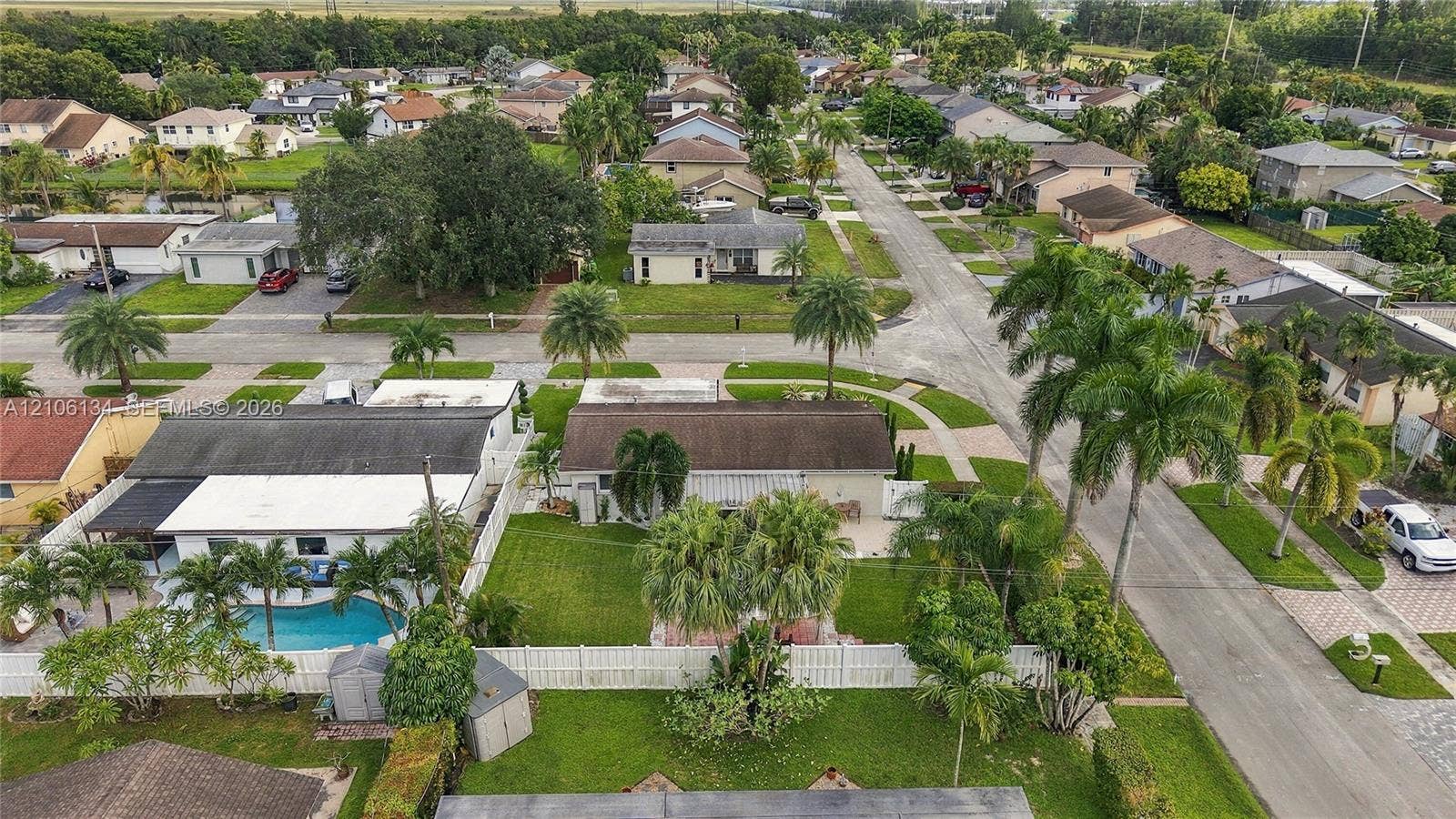 Aerial perspective featuring a residential property with a swimming pool, fenced backyard, and mature palm trees