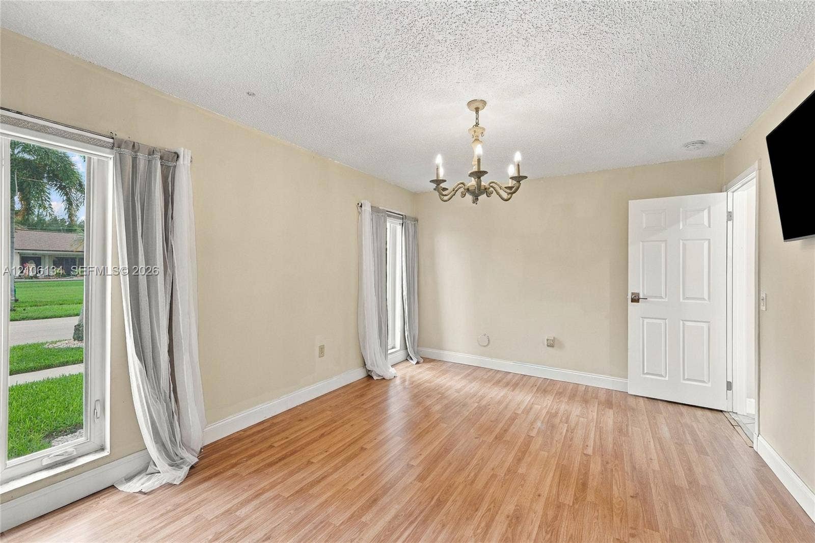 Wood-finish flooring, multi-pane windows with vertical orientation, six-panel interior door, and a multi-arm metallic chandelier