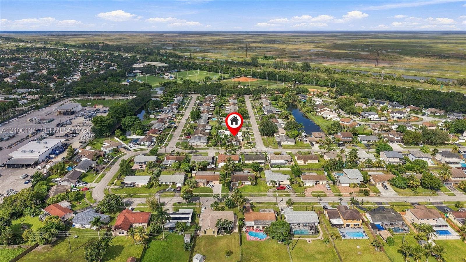 Aerial perspective of the property featuring a suburban lot, paved street access, mature landscaping, and proximity to expansive open green space