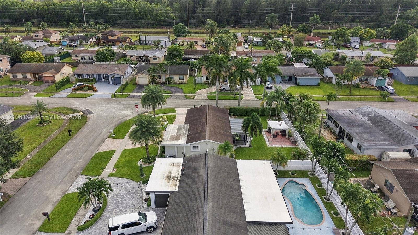 Aerial view of a residential property featuring an in-ground swimming pool, a concrete paver driveway, palm tree landscaping, and a fenced rear yard