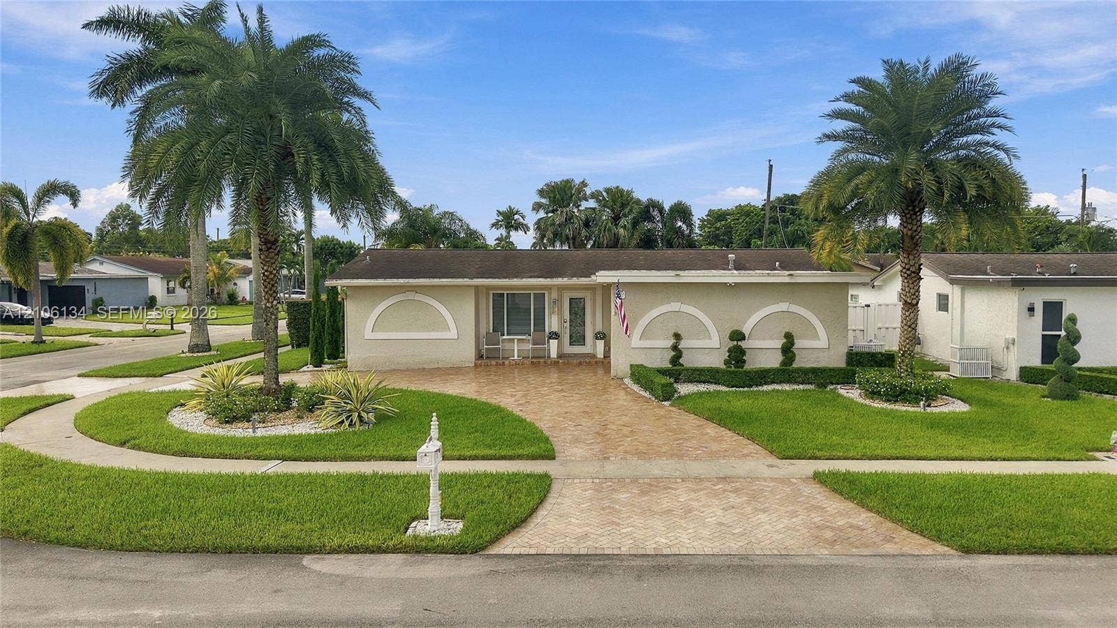 Single-story exterior featuring a decorative concrete driveway, arched wall accents, and established palm trees within the front landscape