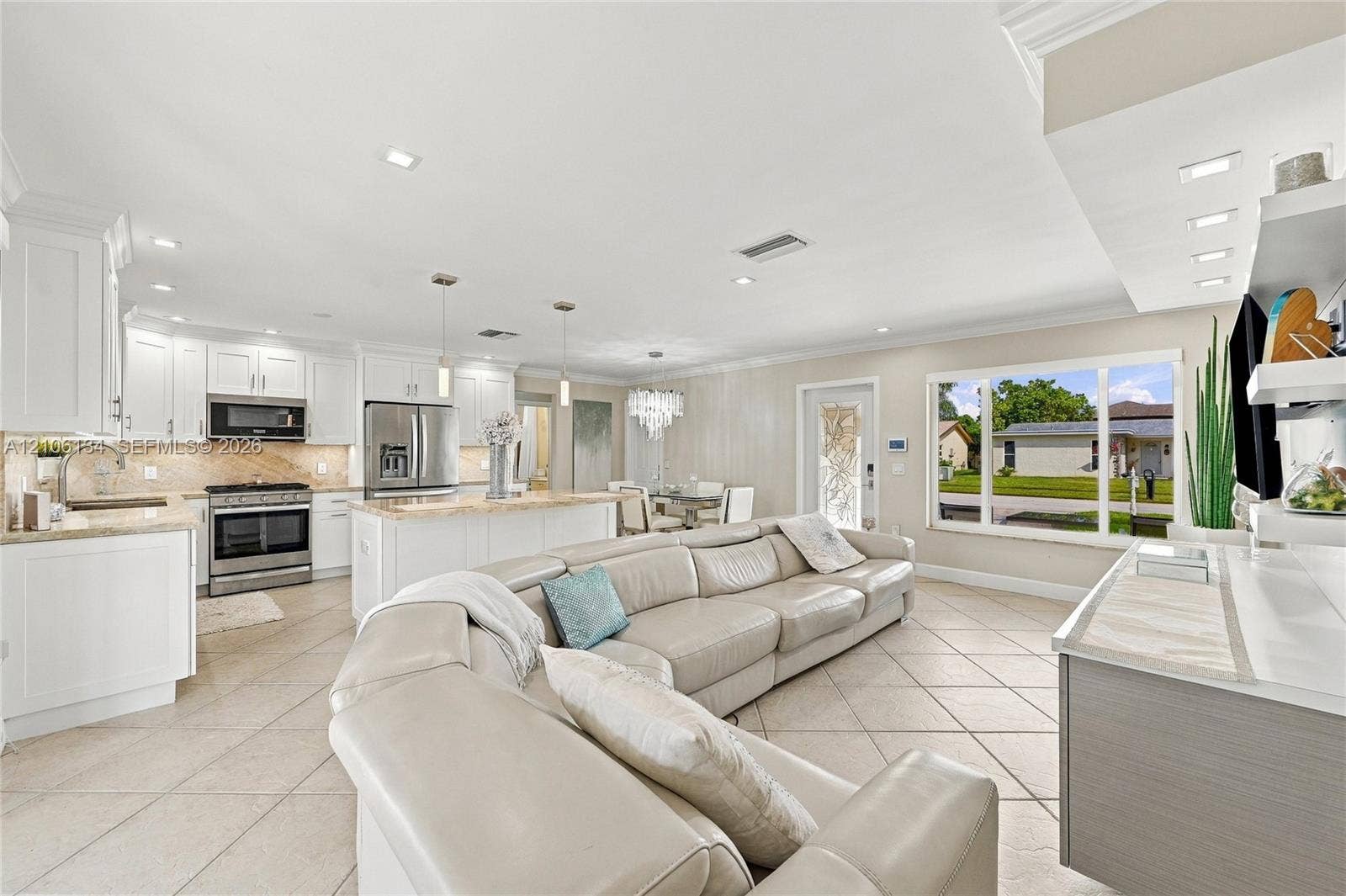Open-concept kitchen featuring white shaker-style cabinetry, stone countertops, stainless steel appliances, recessed lighting, and tile flooring