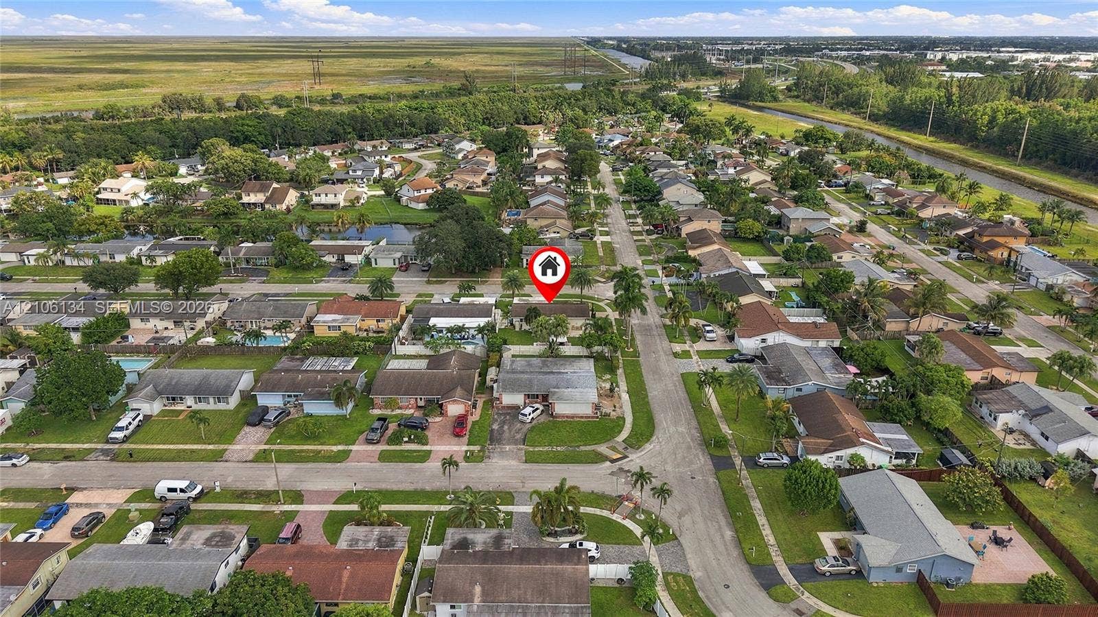 Aerial perspective of a single-story residence situated on a lot with mature landscaping, a paved driveway, and proximity to expansive open green space