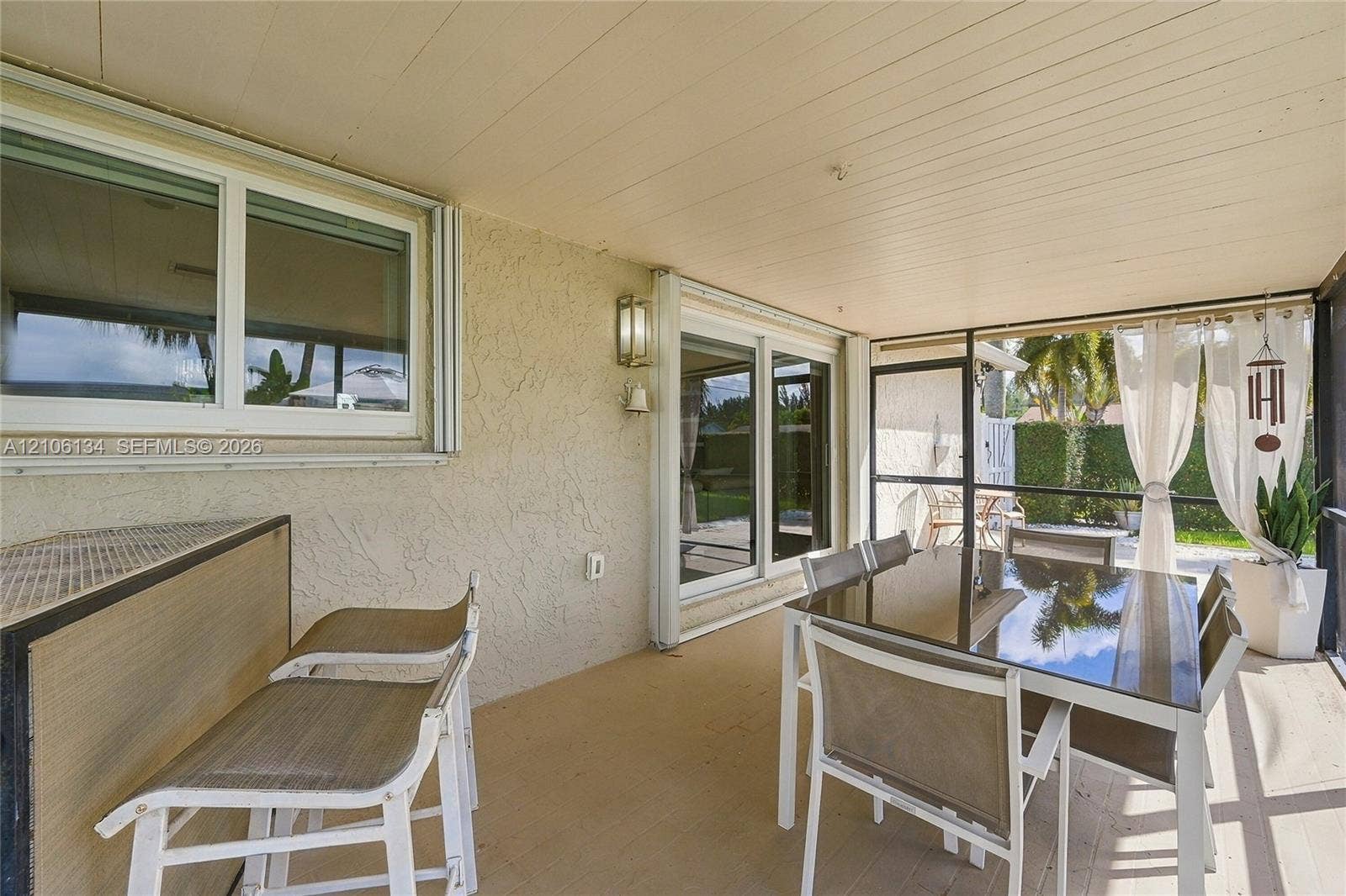 Covered lanai featuring a textured stucco finish, panelled ceiling, dual sliding glass door entryways, and floor-to-ceiling screen enclosure