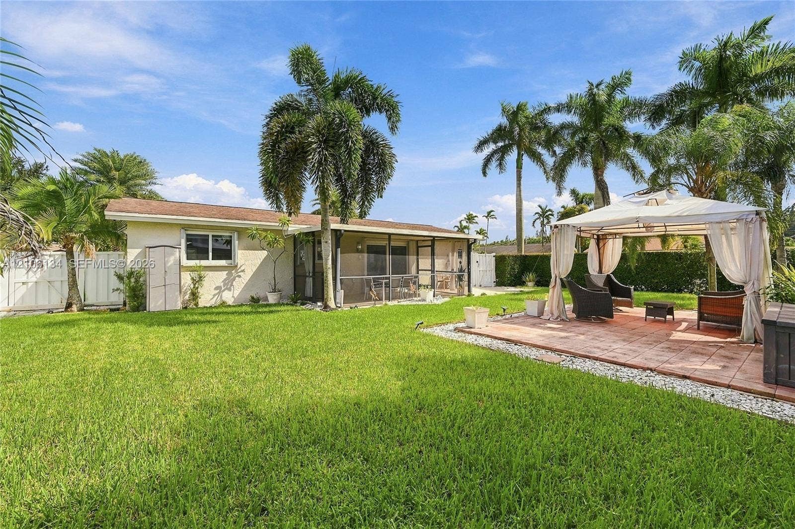 Backyard featuring a paved patio, screen-enclosed porch, mature palm trees, and a white privacy fence