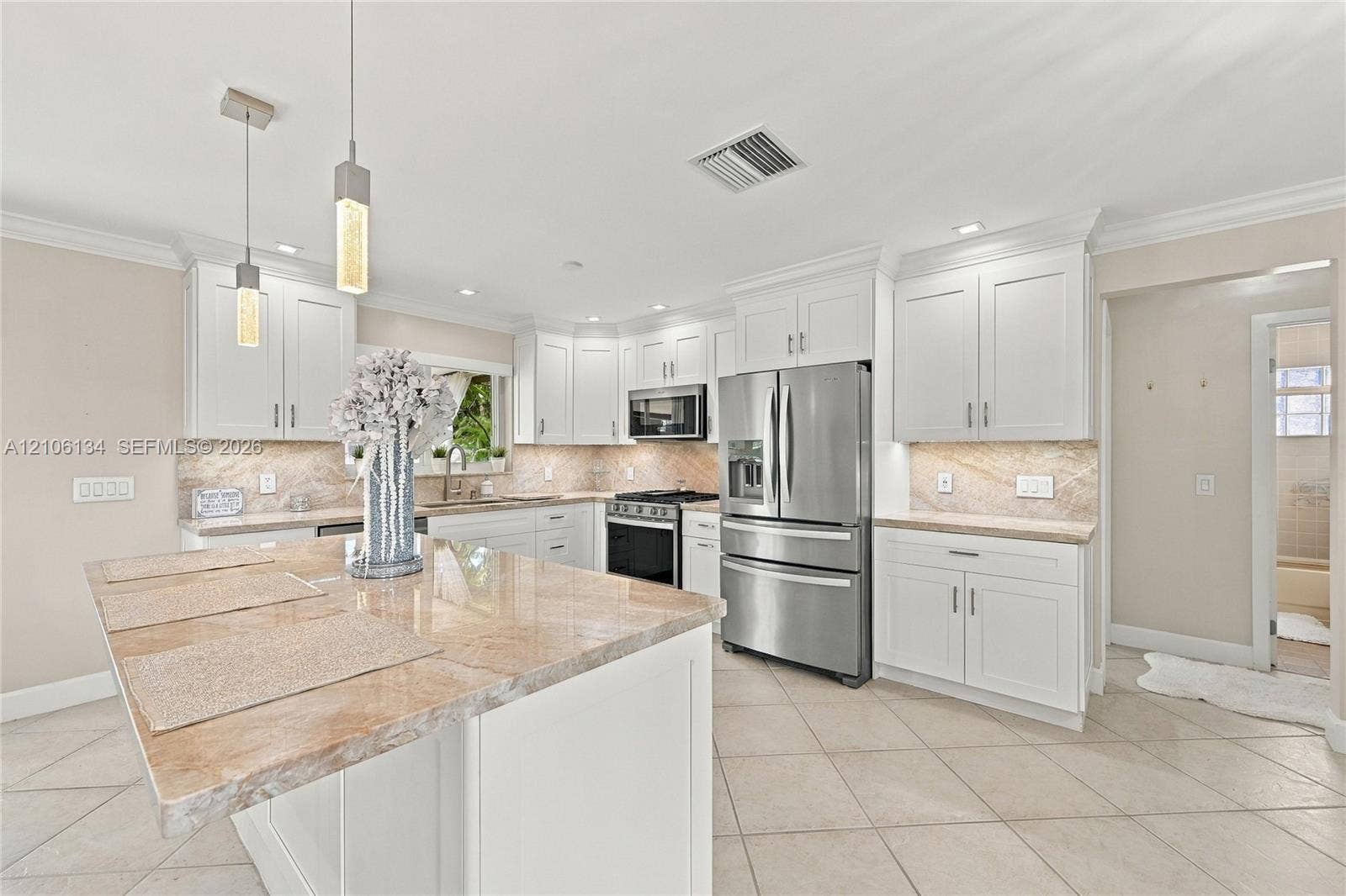 Kitchen featuring white shaker-style cabinetry, stone countertops, central island, stainless steel appliances, and tile flooring