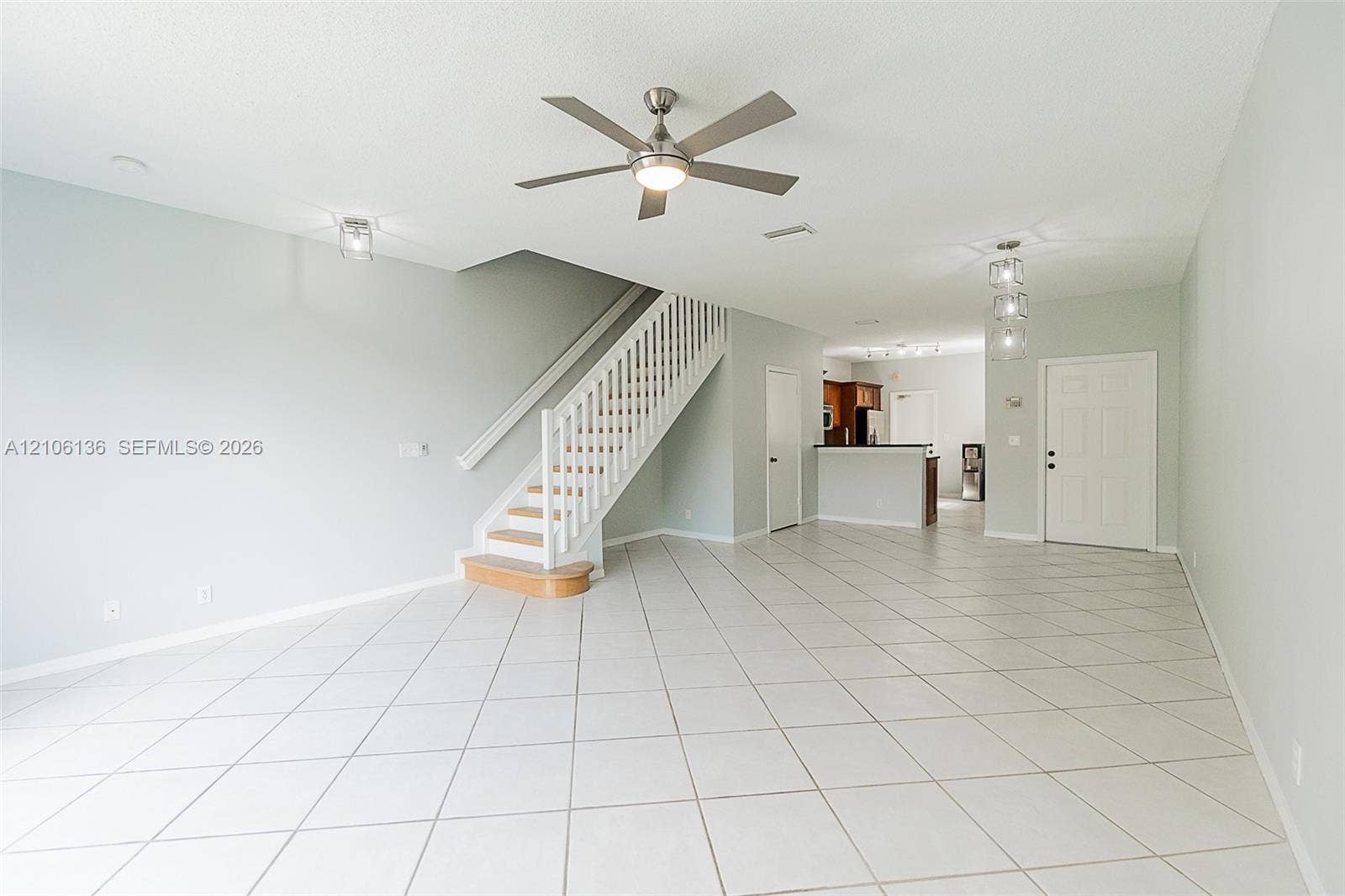 3713 San Simeon Circle, Weston, Weston, FL 33331 Open-concept living space featuring large-format diagonal tile flooring, a brushed-nickel ceiling fan with integrated lighting, a custom staircase with white vertical balusters and a wood-finished bottom tread, and modern multi-pendant lighting