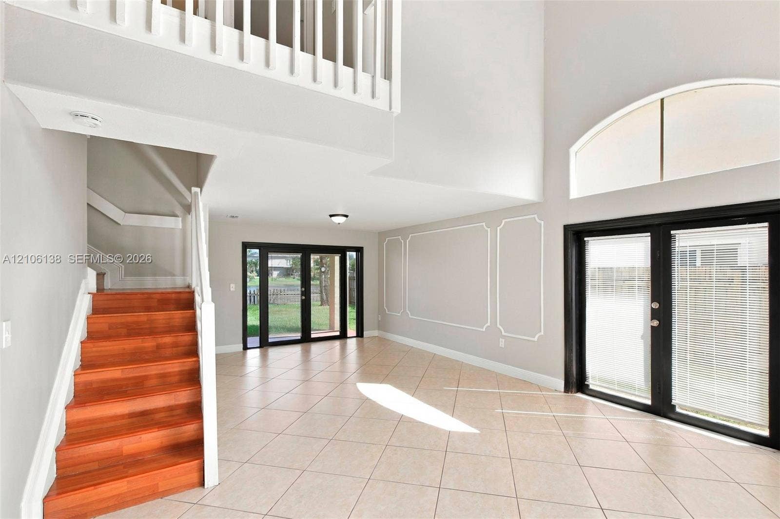 16119 SW 61st Lane, Miami, Miami, FL 33193 Double-height ceiling, open staircase with wood-finish treads, arched transom window, wainscoting wall detailing, and dual sets of glass-paned doors
