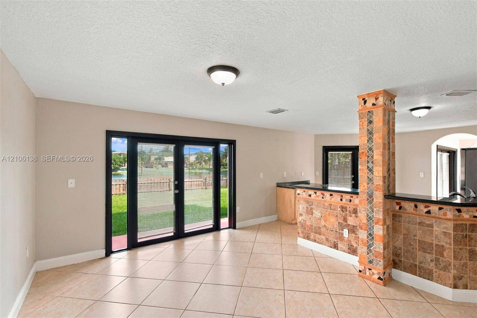 16119 SW 61st Lane, Miami, Miami, FL 33193 Interior space featuring large-format diagonal floor tiles, stone-tiled accent pillar, breakfast bar with dark surface, and black-framed glass french doors