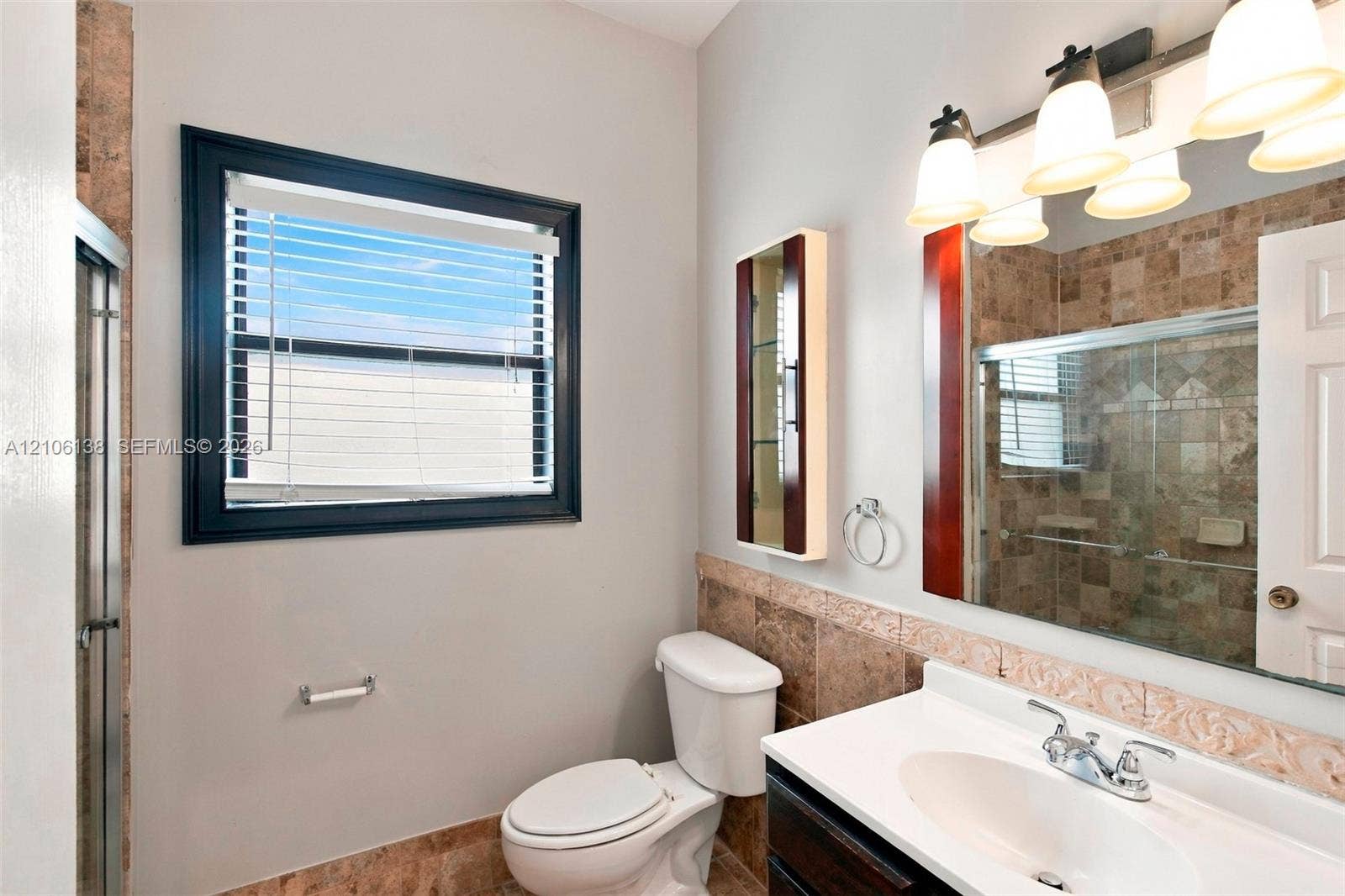 16119 SW 61st Lane, Miami, Miami, FL 33193 Bathroom featuring a single-sink vanity with a solid-surface countertop, tiled shower enclosure, stone-finish wall accents, and a large-format vanity mirror with integrated multi-bulb lighting