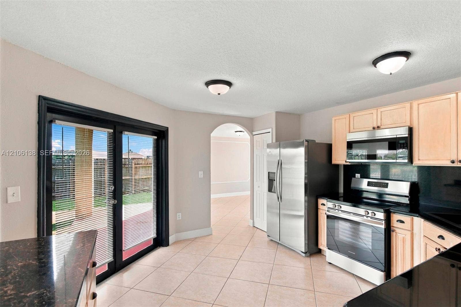 16119 SW 61st Lane, Miami, Miami, FL 33193 Kitchen featuring light-finish cabinetry, black stone-patterned countertops, stainless steel appliances, ceramic tile flooring, and sliding glass doors