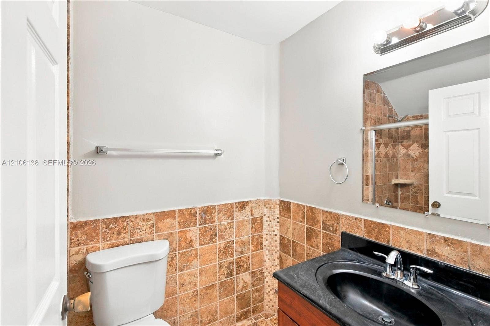 16119 SW 61st Lane, Miami, Miami, FL 33193 Bathroom featuring a wood-tone vanity, dark solid-surface countertop with an integrated oval sink, mid-tone stone tile wainscoting, and a wall-mounted light fixture