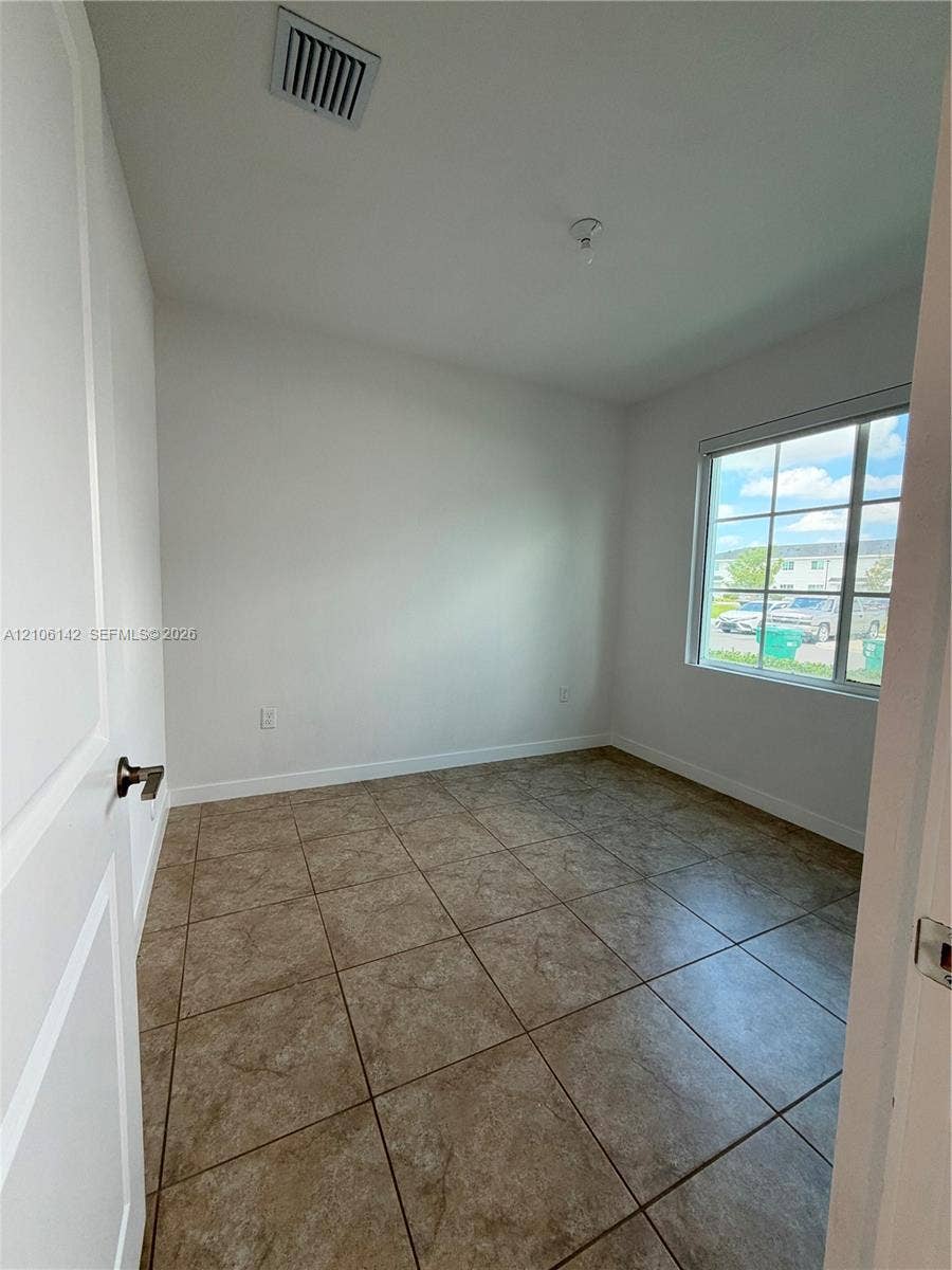 Neutral-toned interior space featuring large-format ceramic tile flooring, a multi-pane window with natural light, and a white paneled interior door