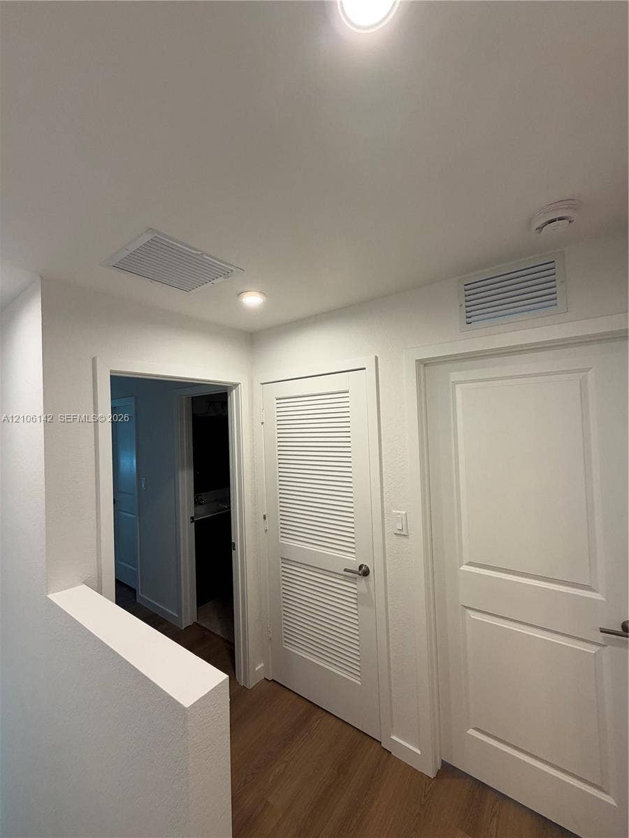 Interior hallway featuring recessed ceiling lighting, louvered closet door, solid-panel interior door, and wood-finish flooring