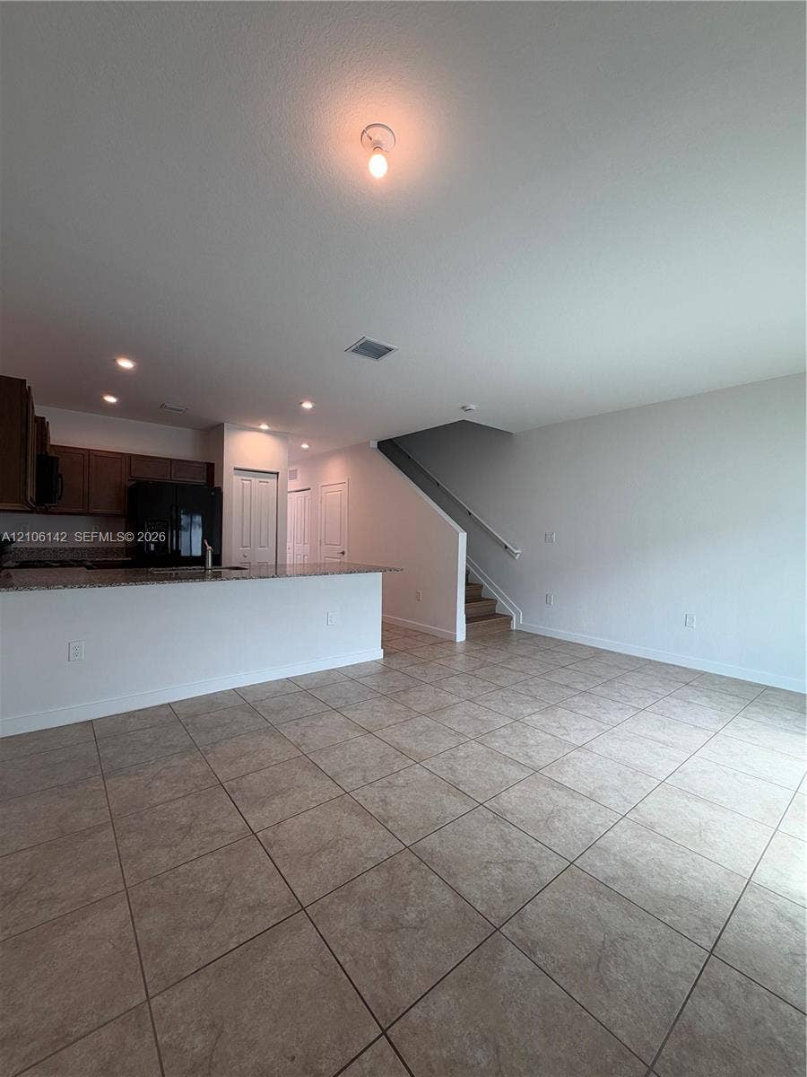 Large-format ceramic tile flooring, kitchen featuring a stone-composite countertop, dark wood-finish cabinetry, built-in staircase with a railing, and recessed ceiling lighting