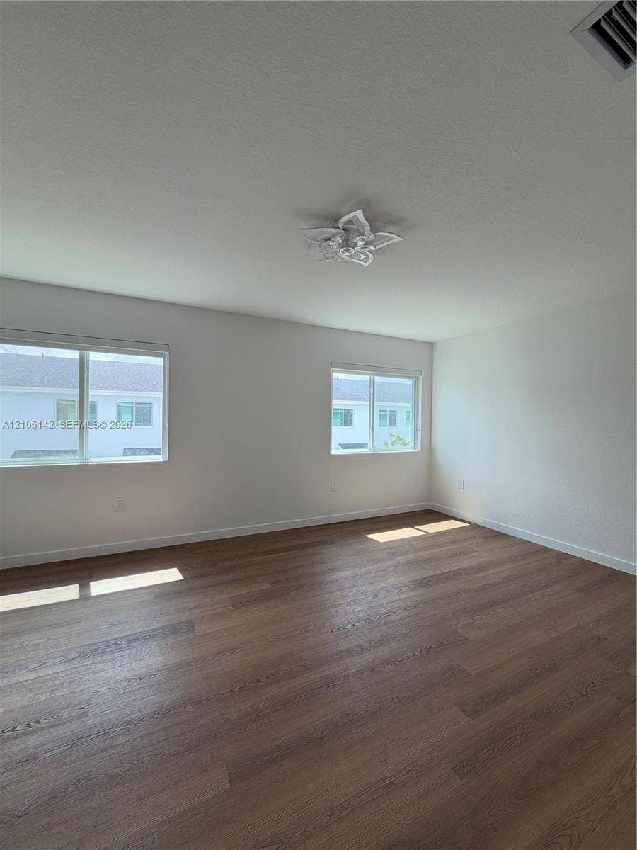 Wood-finish flooring, neutral walls, two windows with white frames, and a multi-bulb overhead light fixture