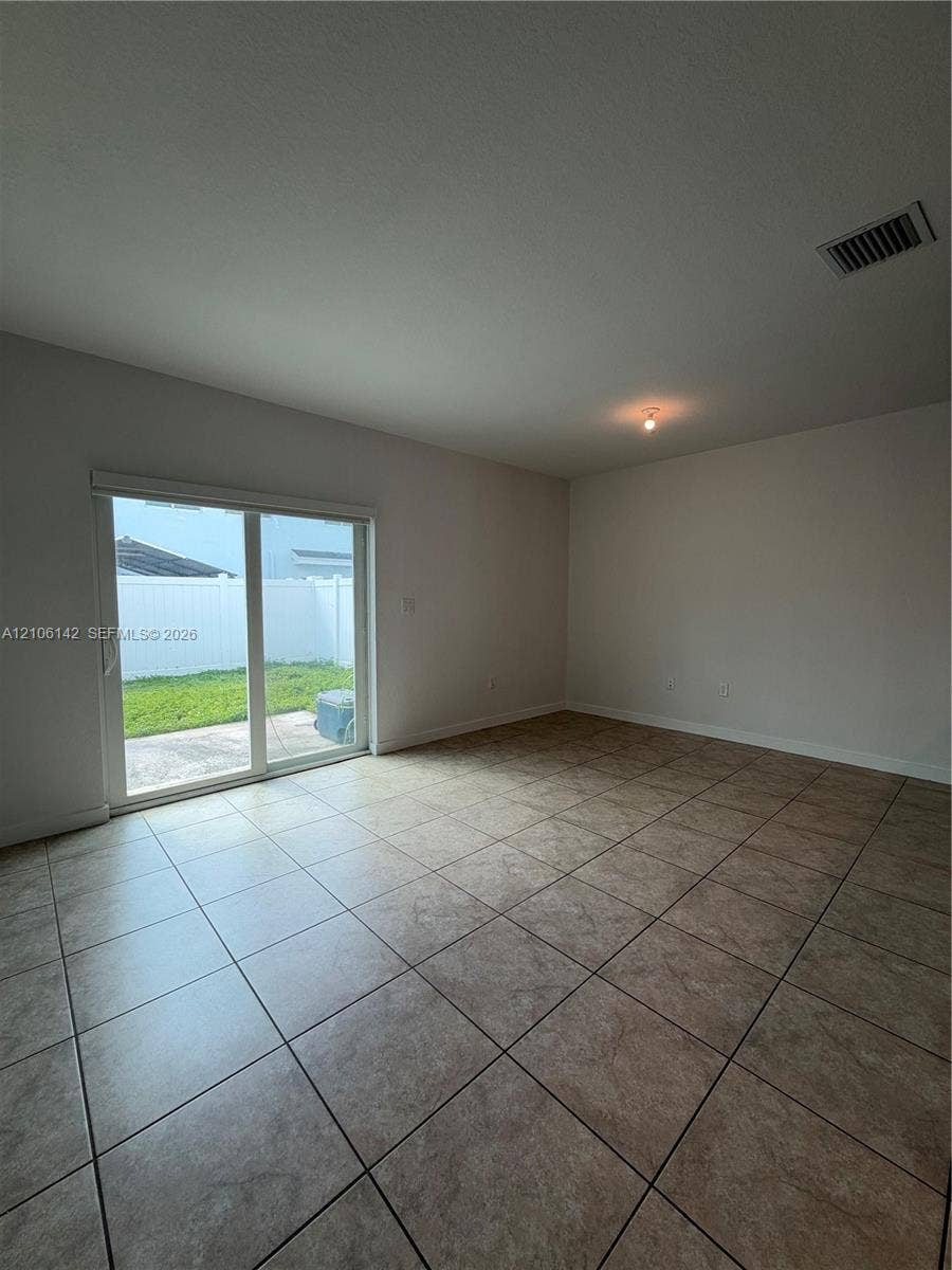 Neutral interior space featuring ceramic tile flooring, sliding glass patio doors, and exterior access to a concrete patio and fenced yard