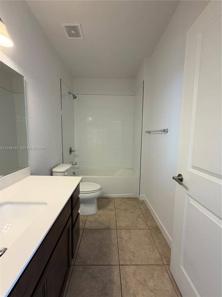 Bathroom featuring a vanity with a white countertop and dark-finish cabinetry, a combination shower and soaking tub with white tile surround, and neutral tile flooring