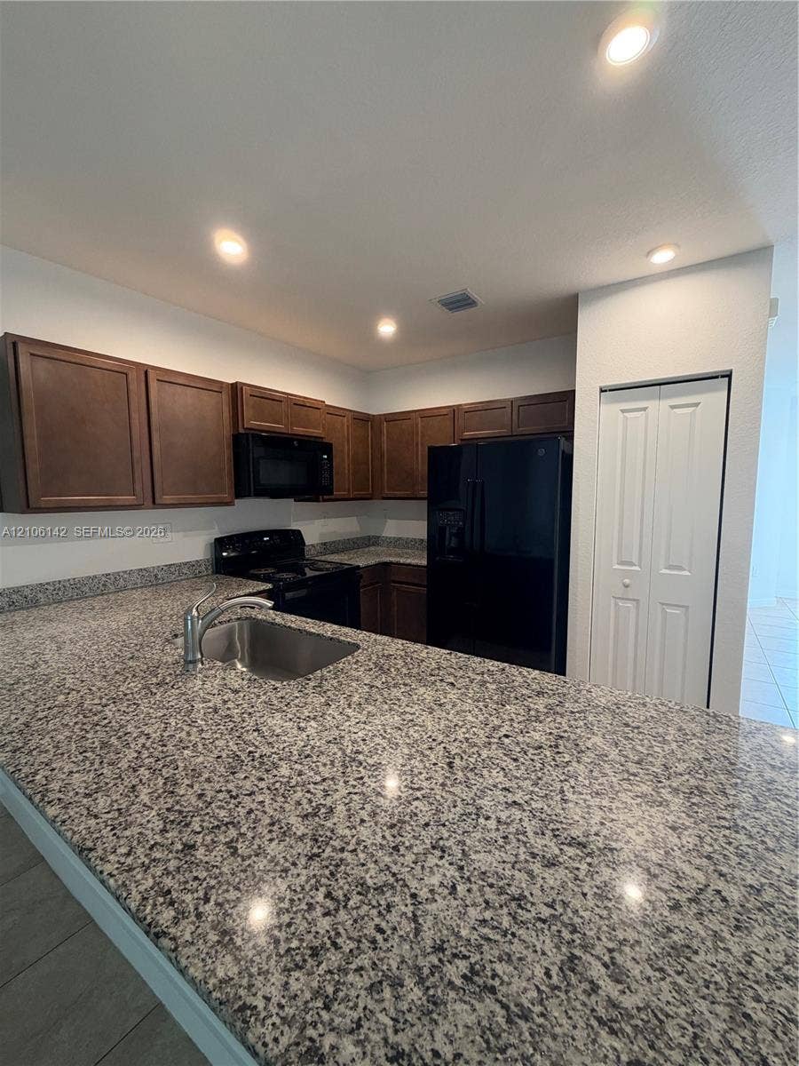 Kitchen featuring stone countertops, dark wood cabinetry, recessed lighting, integrated black appliances, and an undermount stainless steel sink